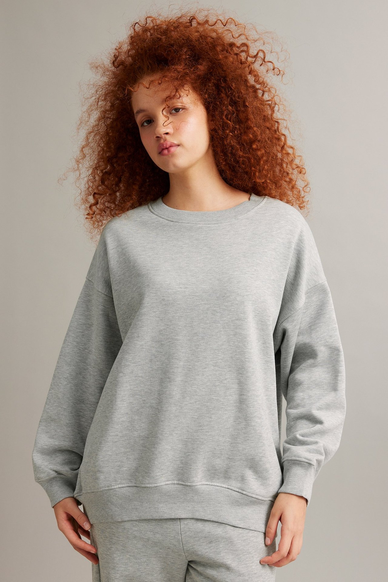 Edestä, nainen yllään vaaleanharmaa meleerattu pitkä collegepaita ja yhteensopivat collegehousut.