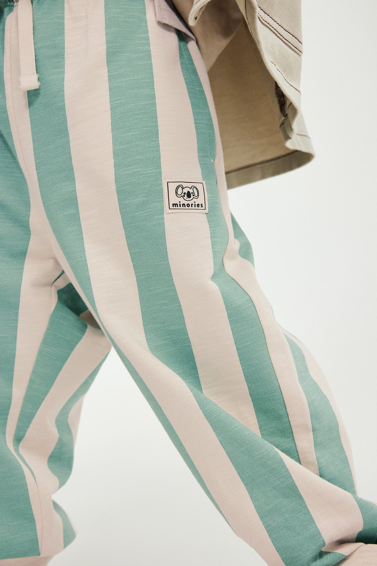 Lapsi yllään vihreät ja vaaleanbeiget raidalliset puuvillahousut kiristysnyörillä ja beige paita.