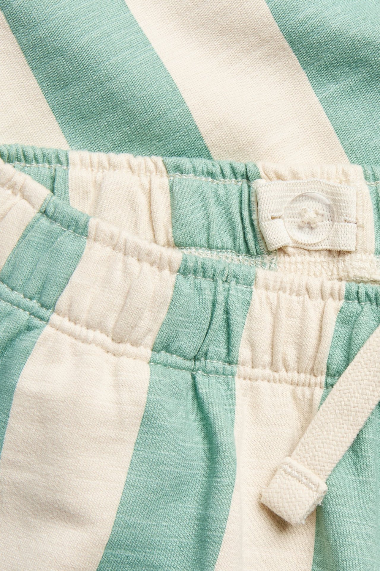 Lähikuva: Vihreä-valkoraidalliset verryttelyhousut, joissa joustava, säädettävä vyötärö ja kiristysnyöri.