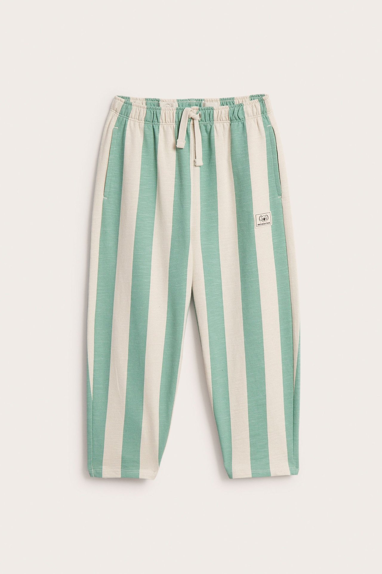 Edestä näkymä lasten vihreä- ja luonnonvalkoraidallisista puuvillahousuista sivutaskuilla ja koristenyörillä.