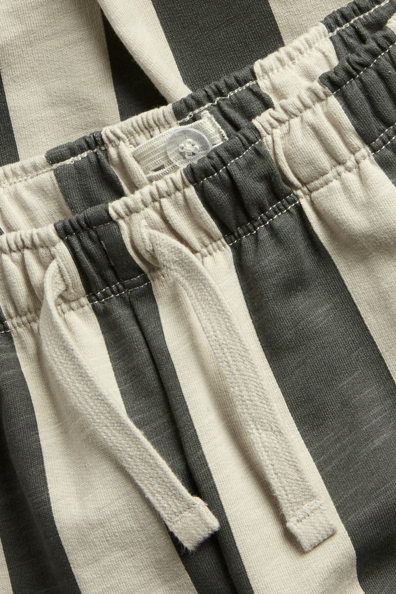 Närbild av barnens mörkgrå och ljusbeige randiga joggingbyxors linning med dragsko.