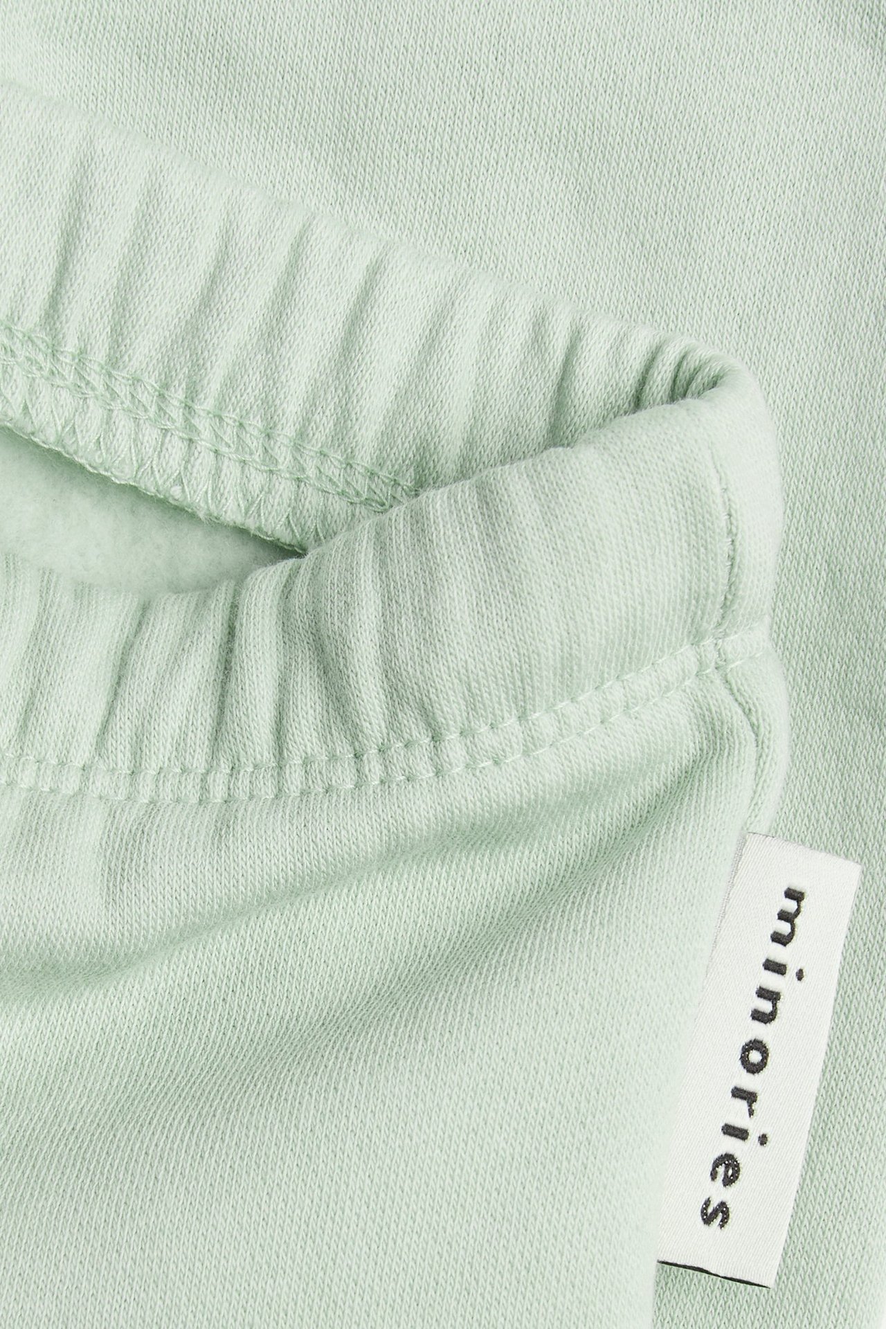 Närbild av bebisens gröna bomullsmix mjukisbyxor, visar resårbandad midja och en liten etikett.