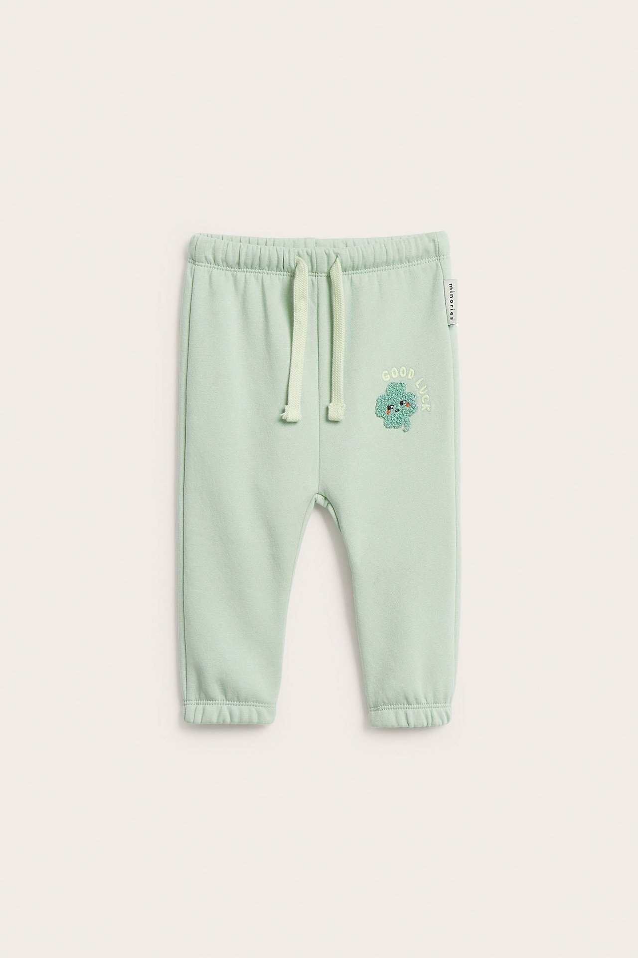 Frontvy av babygröna mjukisbyxor i bomullsblandning med klöverapplikation och dragsko i midjan.