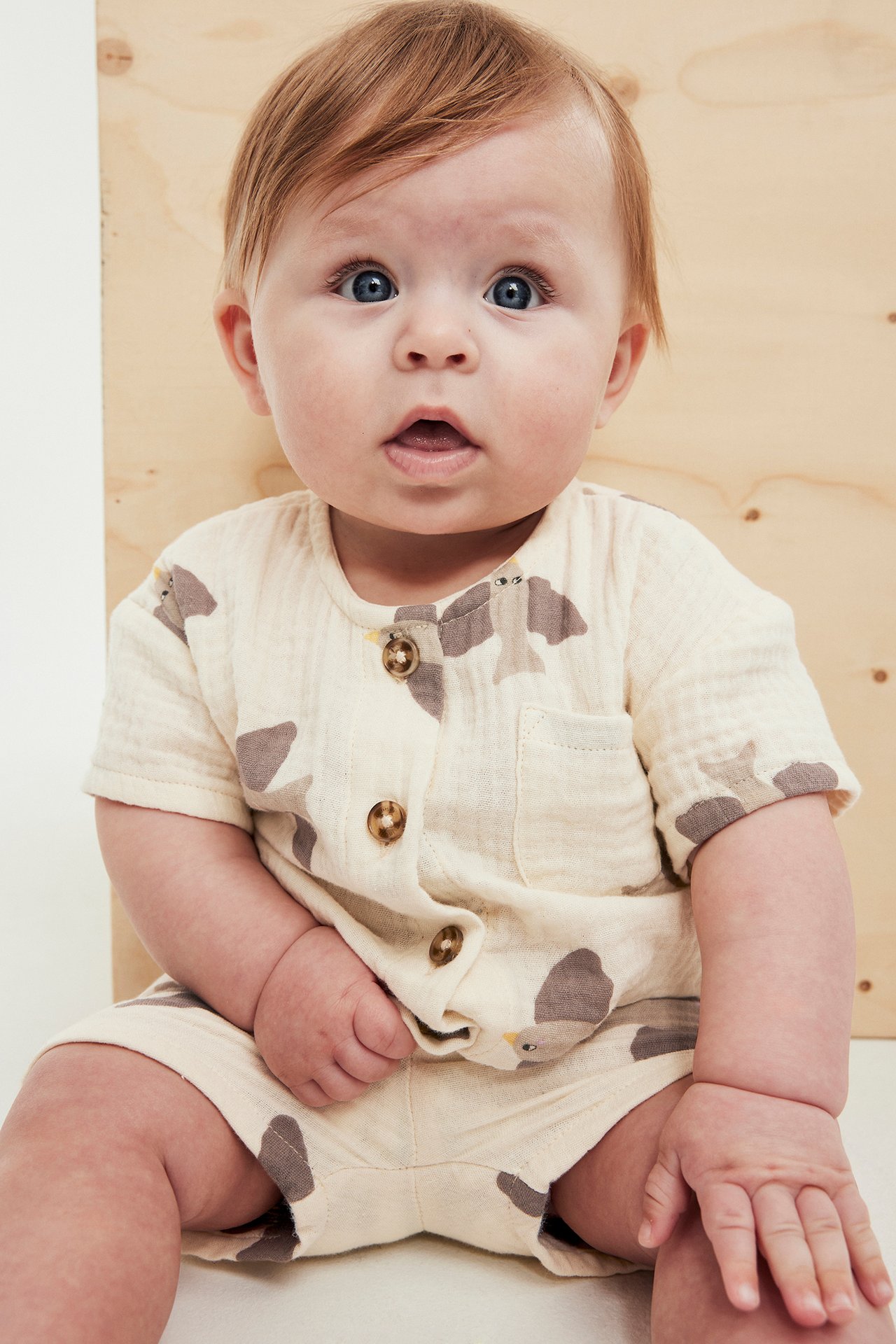 Forfra, baby i beige musselin kortermet skjorte med brunt fuglemønster og matchende shorts.