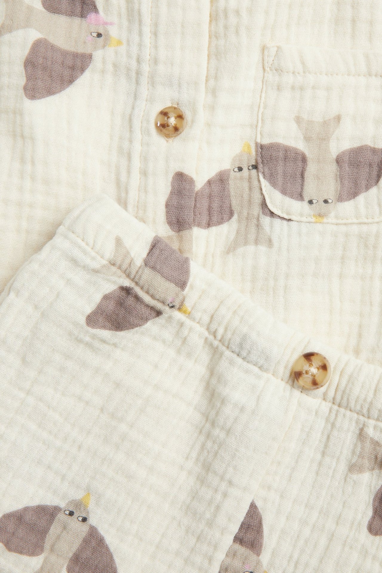 Zbliżenie beżowego, wzorzystego zestawu niemowlęcego z muślinu: koszula z guzikami i kieszenią, oraz szorty.