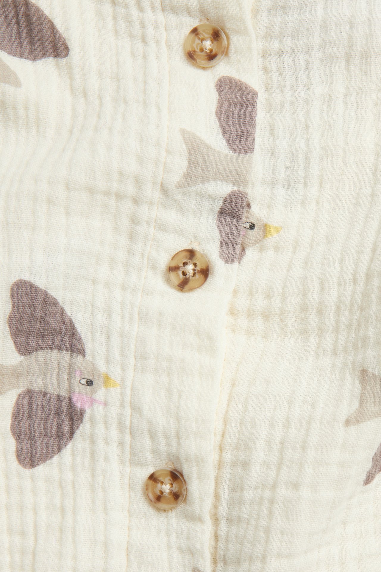 Lähikuva beigestä puuvillamusliinipaidasta, jossa on vaaleanruskea lintukuvio ja ruskeat napit.