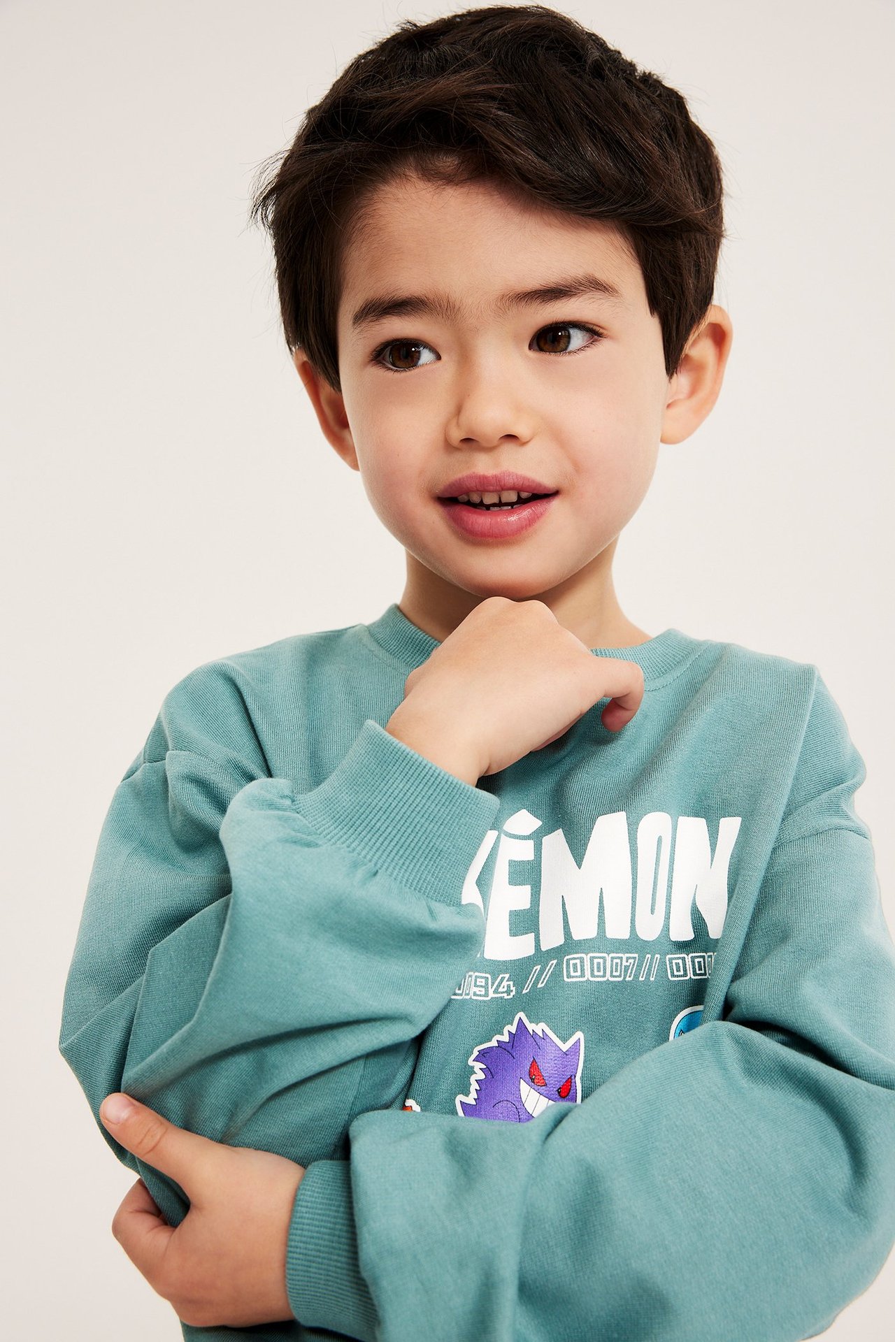 Närbild framifrån på ett barn i en ljusgrön bomullssweatshirt med Pokémon-tryck.