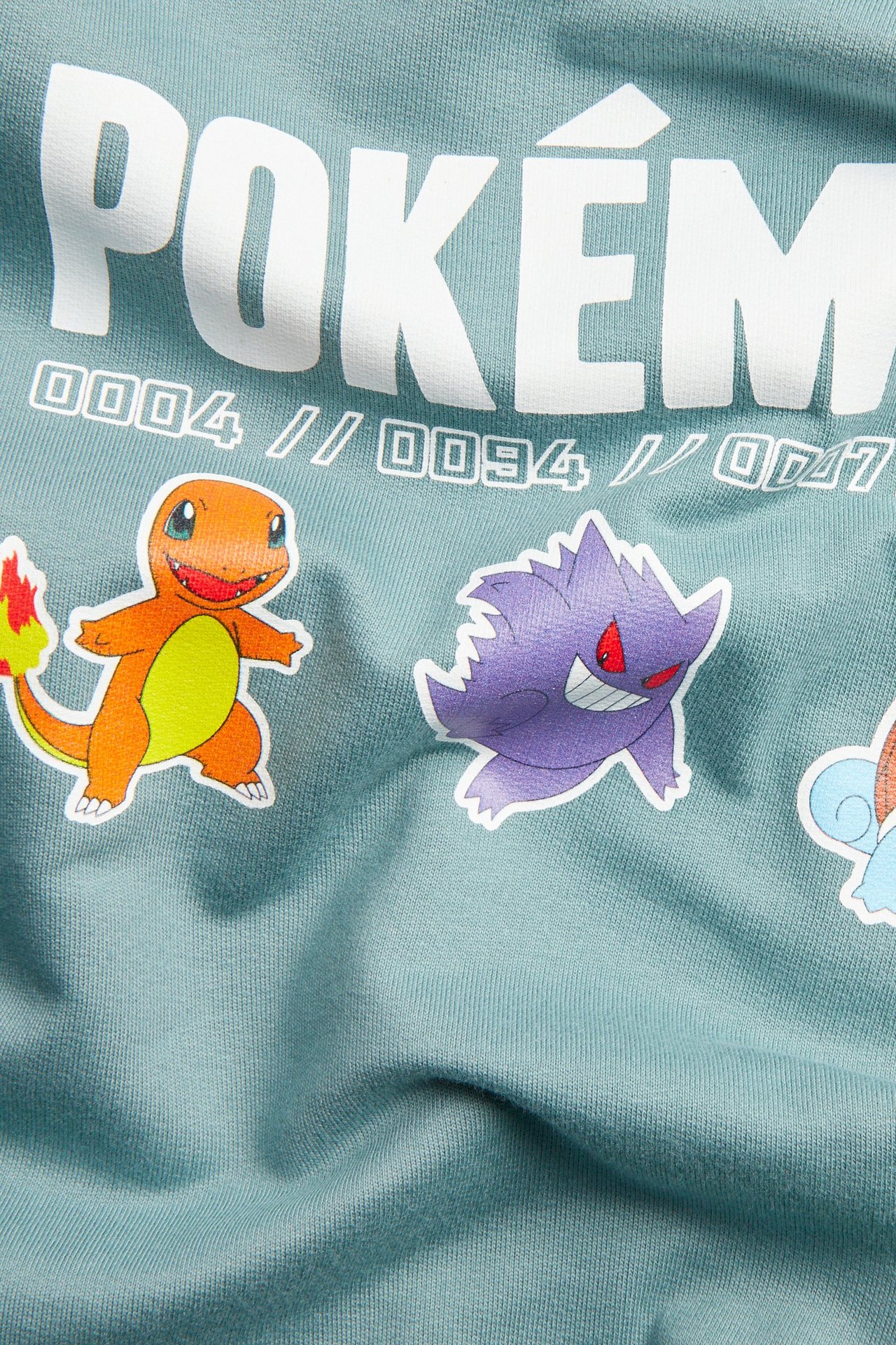 Närbild på en ljusgrön bomullströja med vitt POKÉMON-tryck och karaktärstryck framtill.