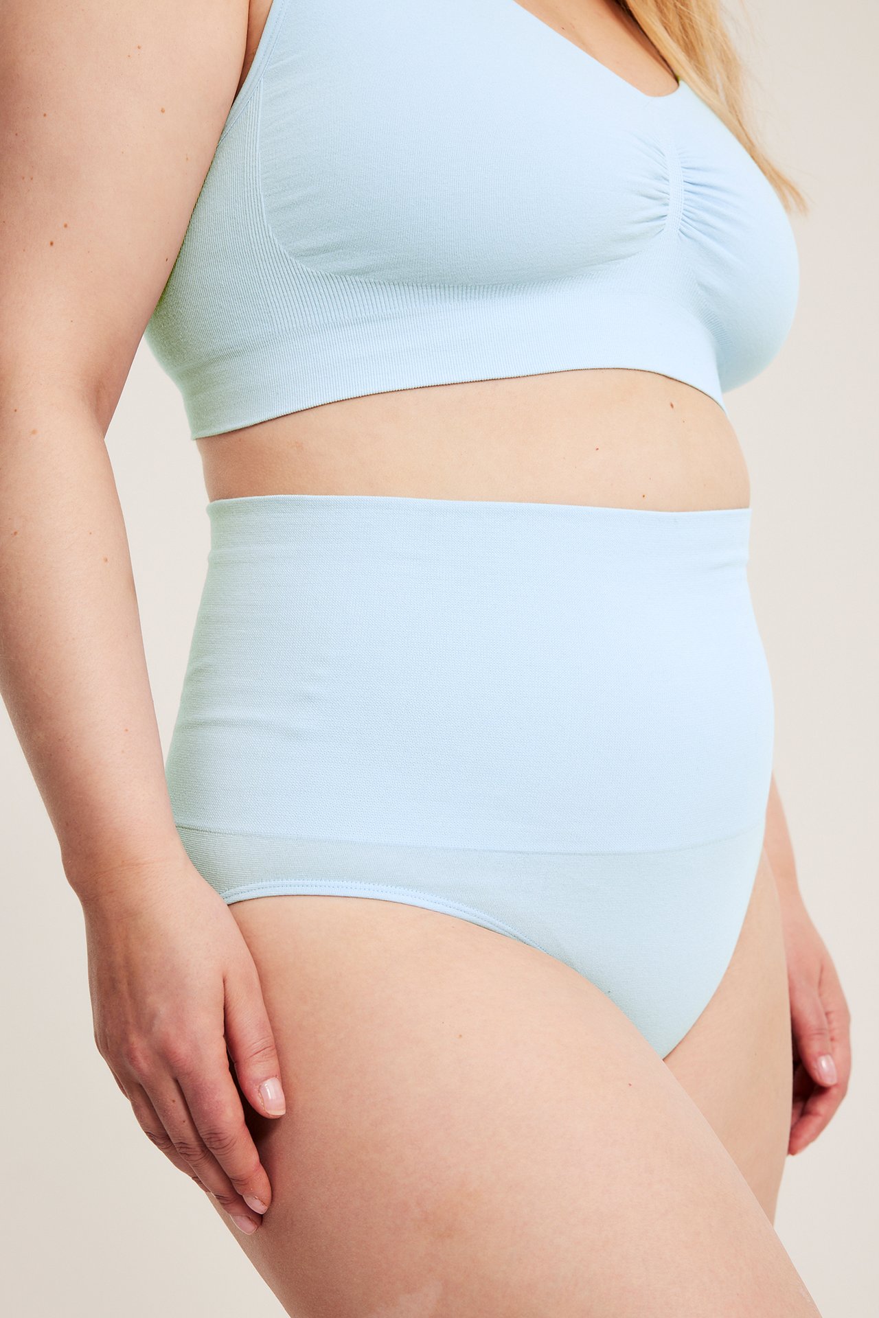 Sidevisning av kvinne i lyseblå sømløs truse med ekstra høyt liv og matchende sømløs BH.
