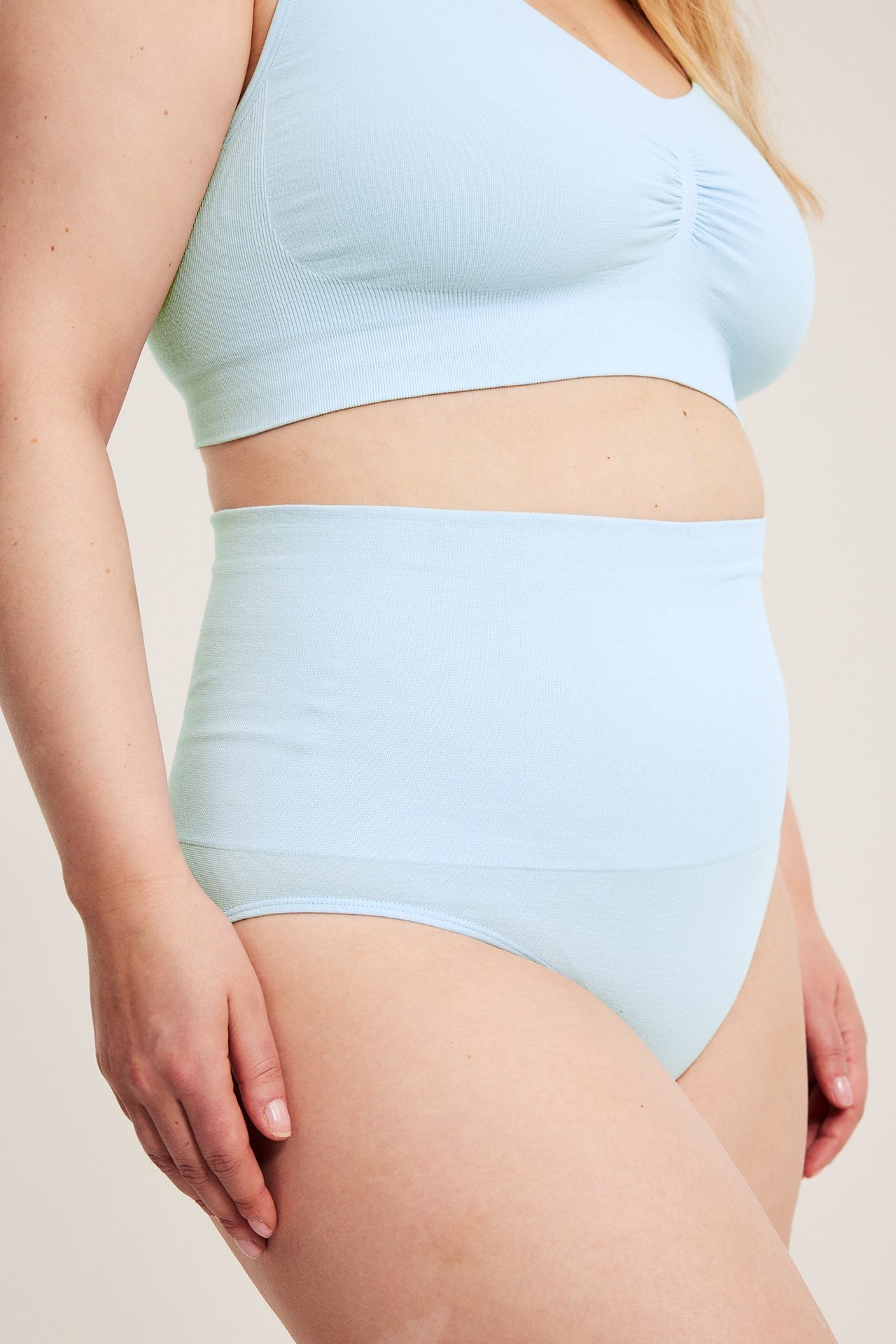 Sidevisning av kvinne i lyseblå sømløs truse med ekstra høyt liv og matchende sømløs BH.