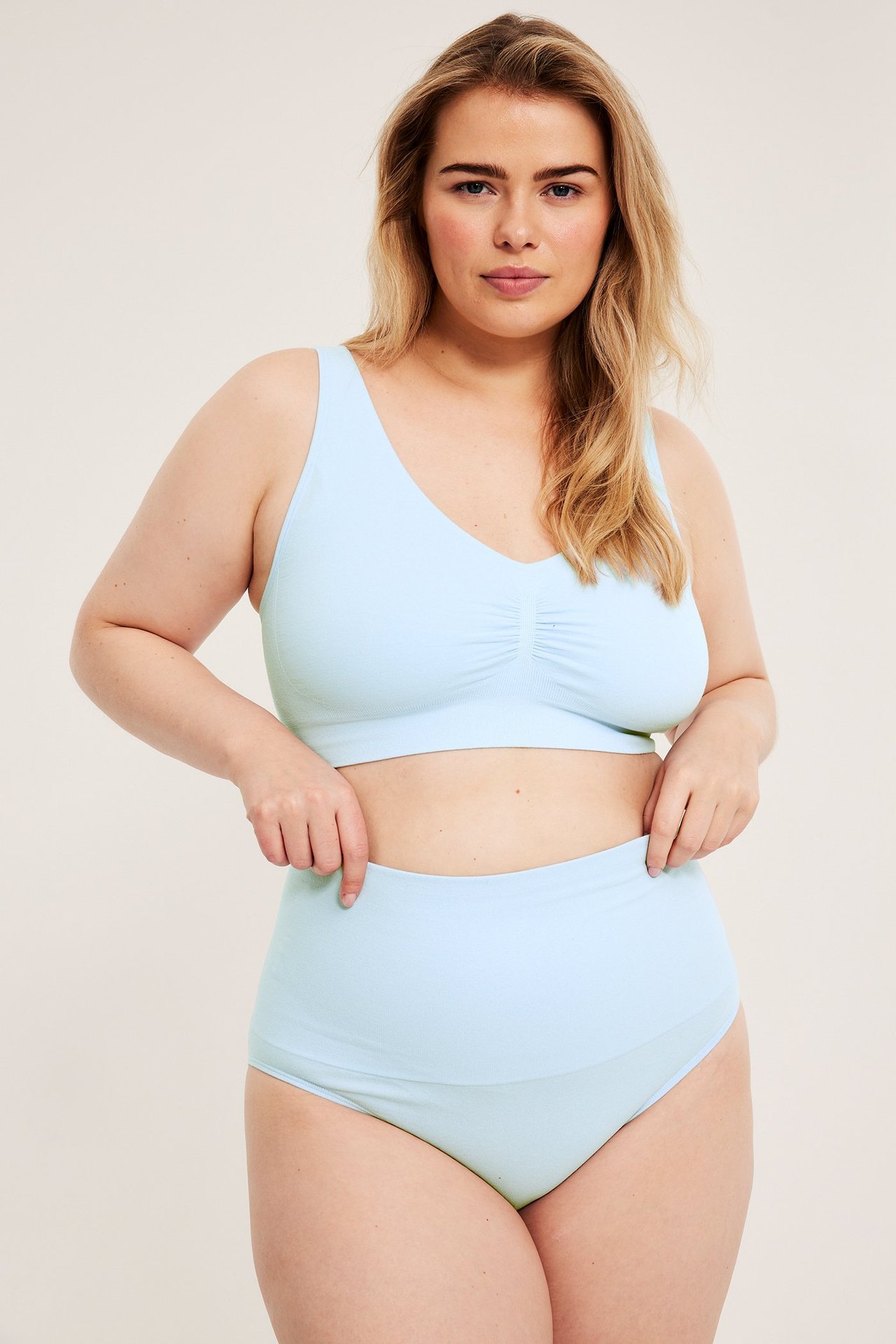 Frontbilde: kvinne i lyseblå sømløs høy midje truse og matchende BH, holder i trusekanten.
