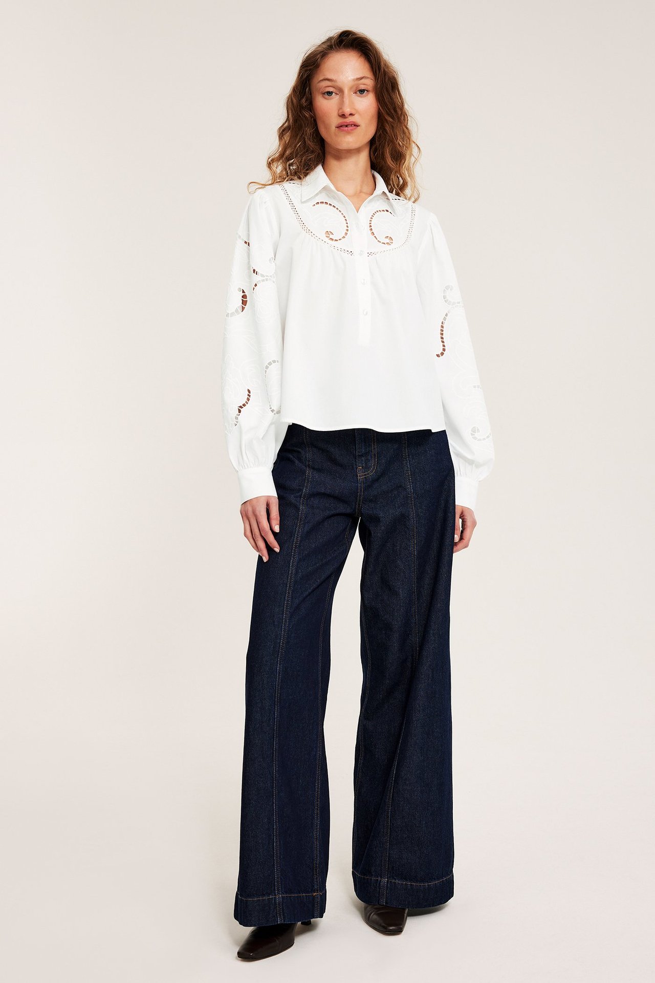 Frontutsikt: Kvinne har på seg en hvit brodert bomullsbluse, stylet med mørkeblå vide jeans.