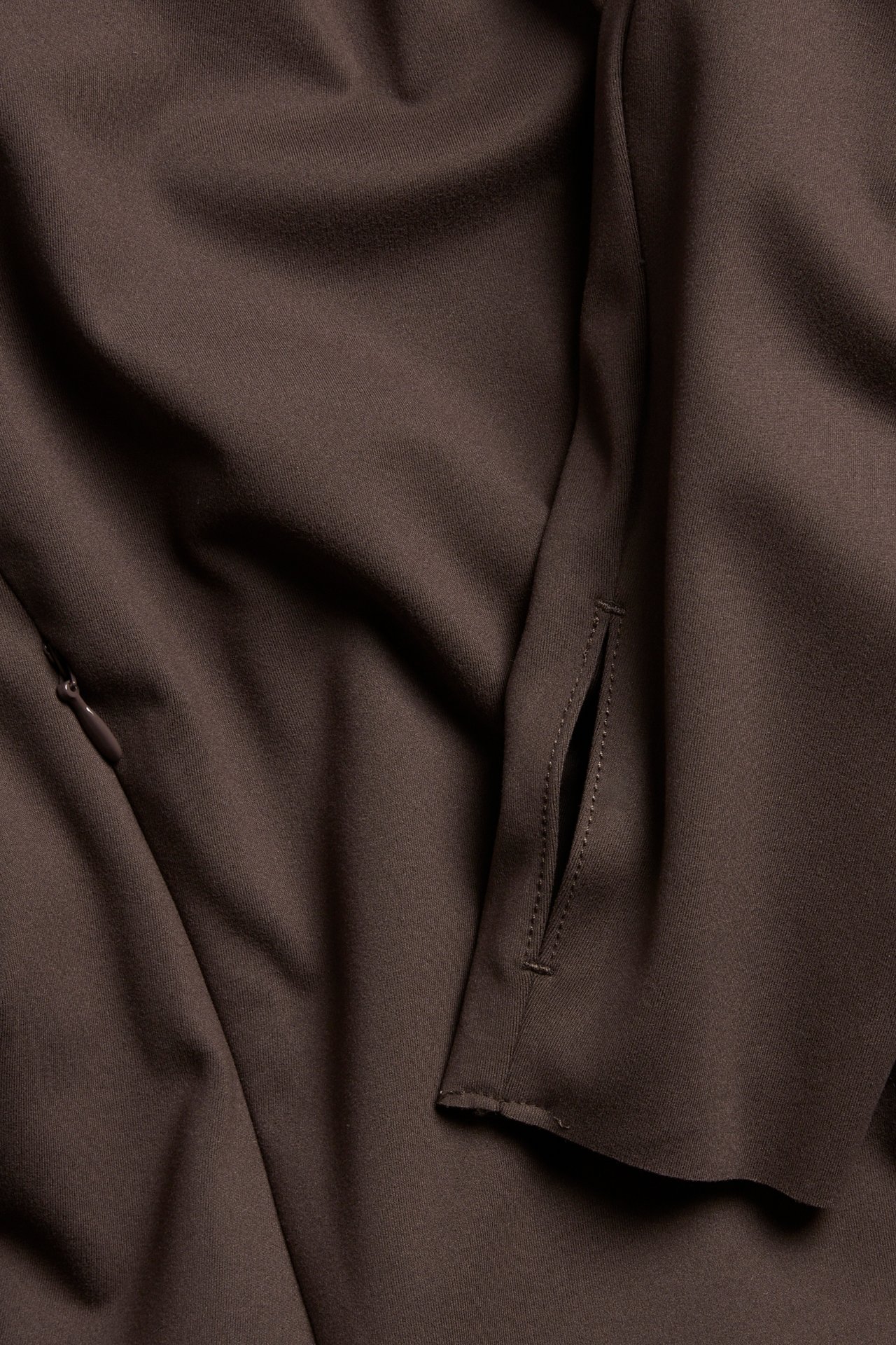 Närbild av en brun enfärgad träningsjacka med dragkedjeficka och tumhål.