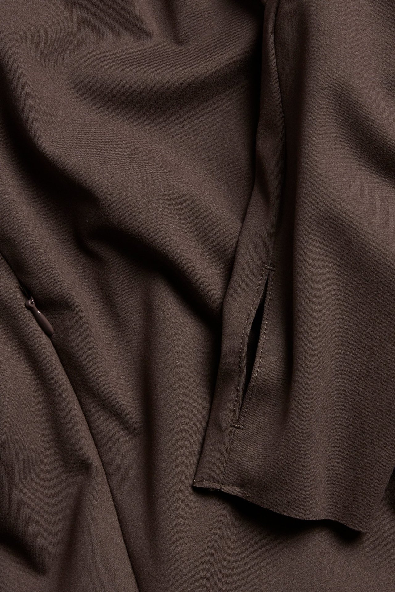 Zbliżenie na brązową jednolitą kurtkę treningową z kieszenią na zamek i otworem na kciuk.