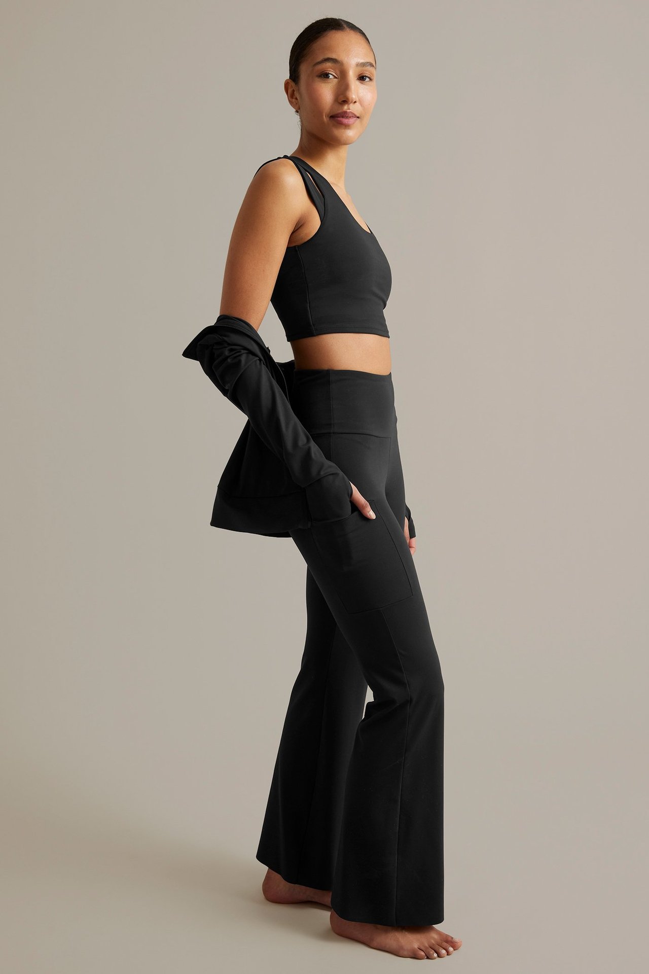 Sidovy av kvinna i svarta bootcut träningstights med mobilficka, sport-bh och jacka över axlarna.