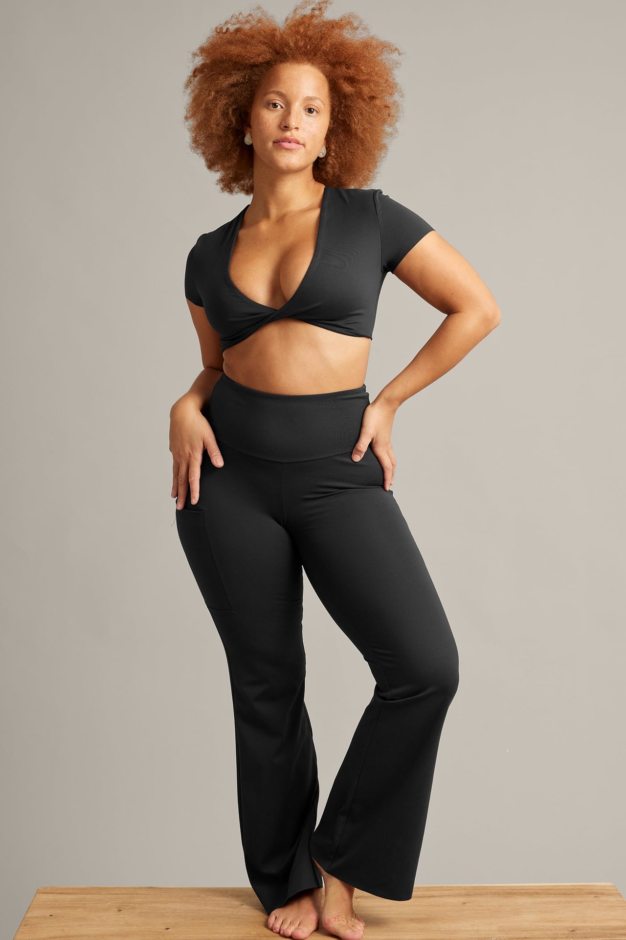 Framifrån: Kvinna i svarta utsvängda leggings med ficka och svart vriden crop top.