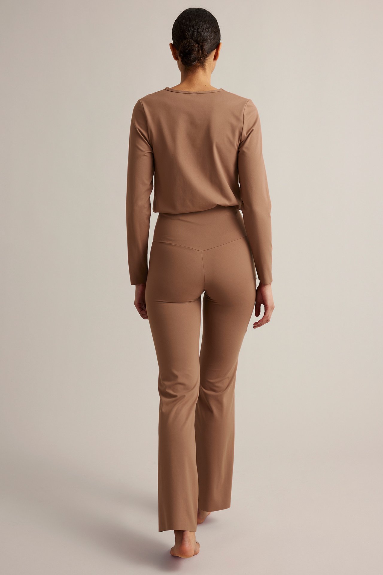 Bakifrån en kvinna i bruna high-waist bootcut träningstights och matchande långärmad topp.