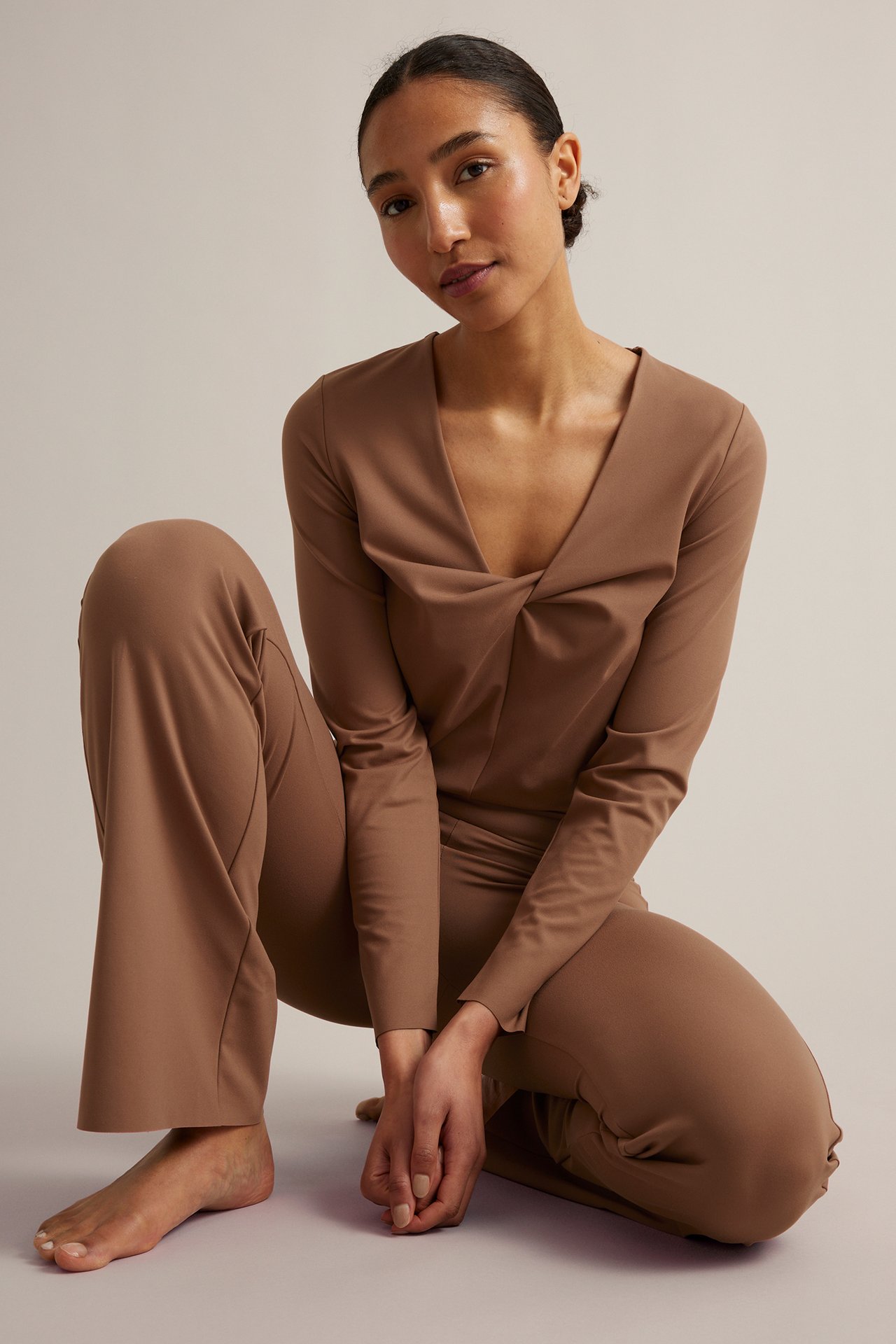 Framifrån, kvinna i bruna stretchiga bootcut träningstights och matchande långärmad topp.