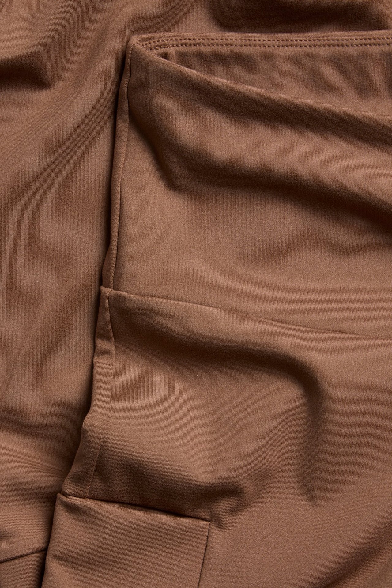 Zbliżenie brązowych legginsów treningowych, ukazujące gładki materiał z poliestru i elastanu oraz szwy.