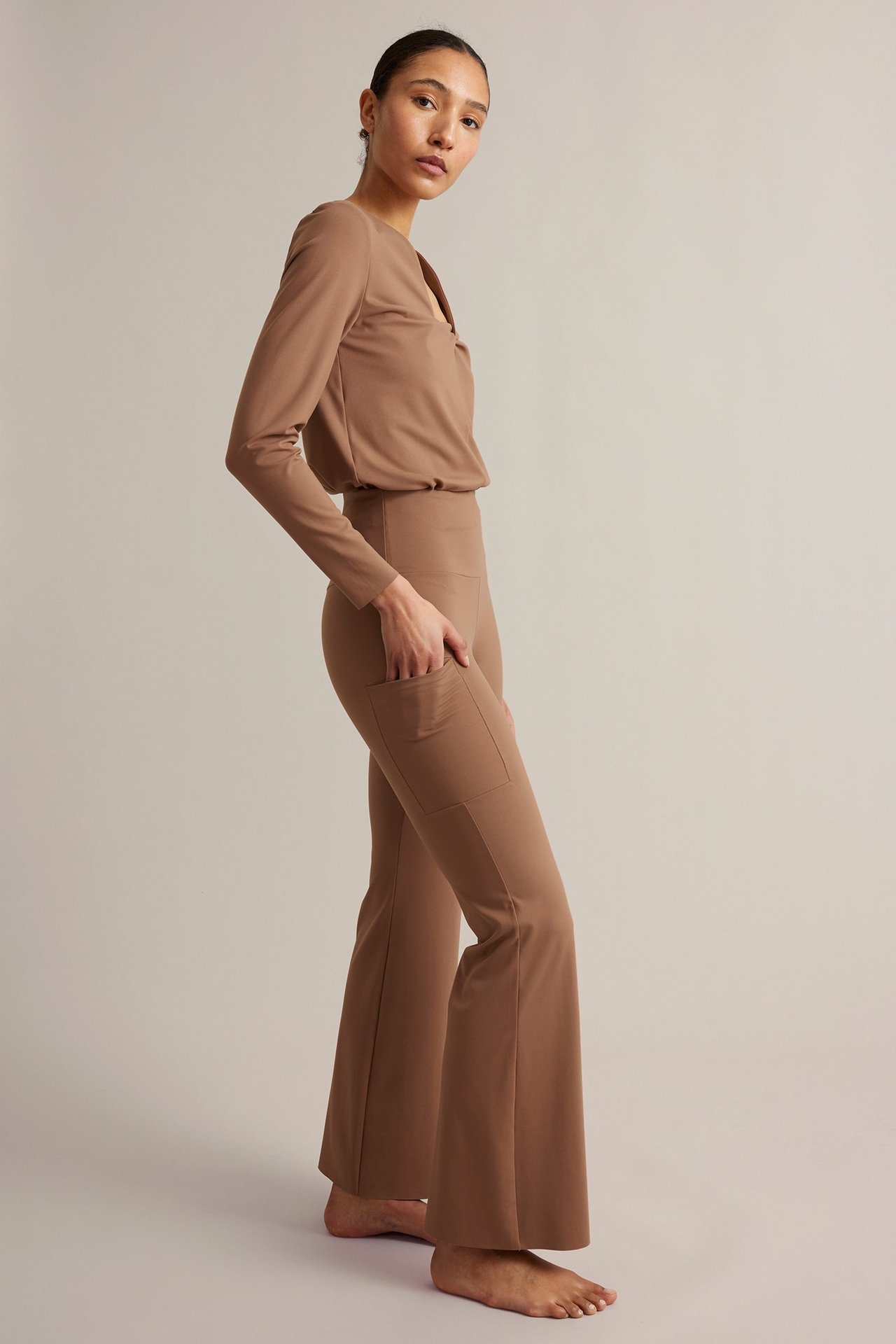 Widok z boku, kobieta w brązowych legginsach treningowych bootcut z wysokim stanem i kieszenią, dopasowana bluzka.