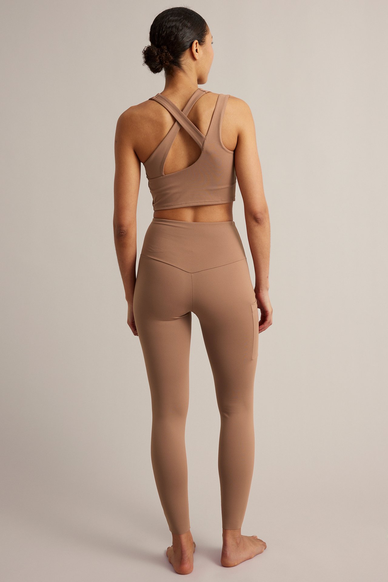 Ryggvy av kvinna i högmidjade beige träningstights med sidoficka och matchande sport-bh.