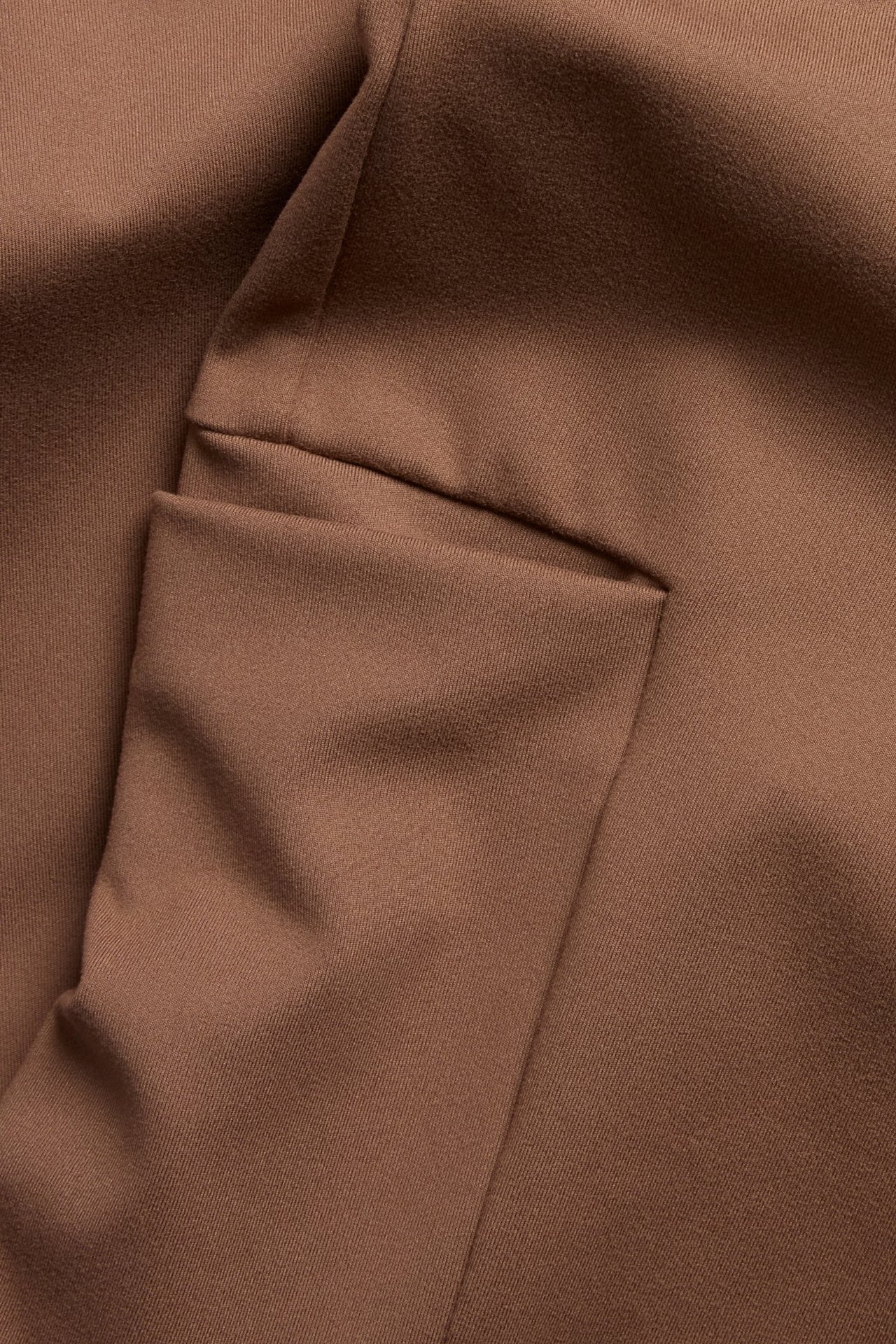 Zbliżenie brązowych legginsów treningowych, pokazujące miękki materiał i boczną kieszeń na nogawce.