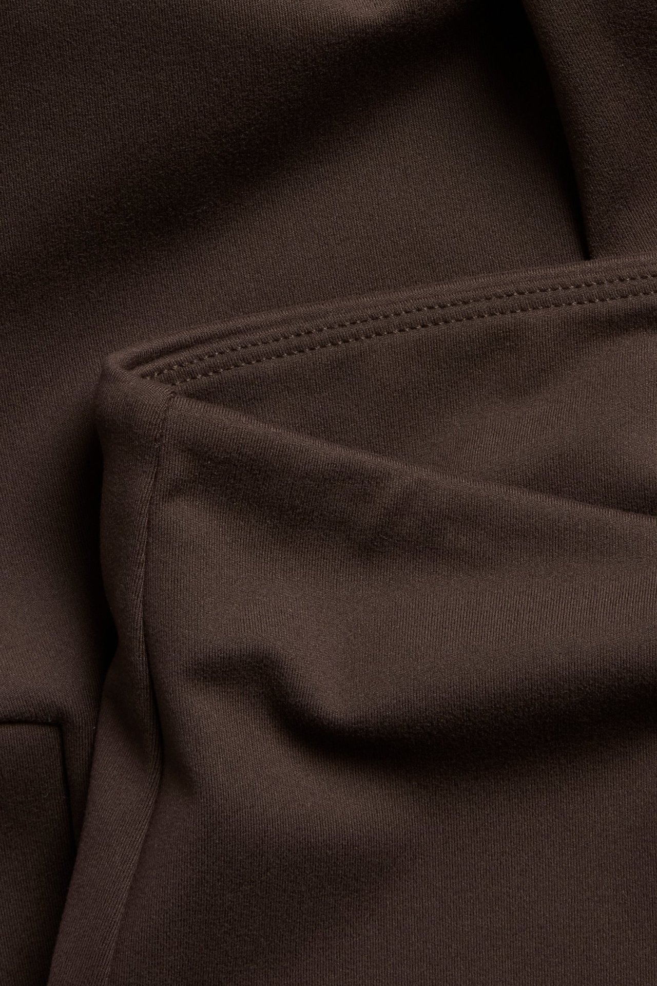 Zbliżenie na brązowe legginsy treningowe, pokazuje miękką powierzchnię, widoczny szew i boczną kieszeń.