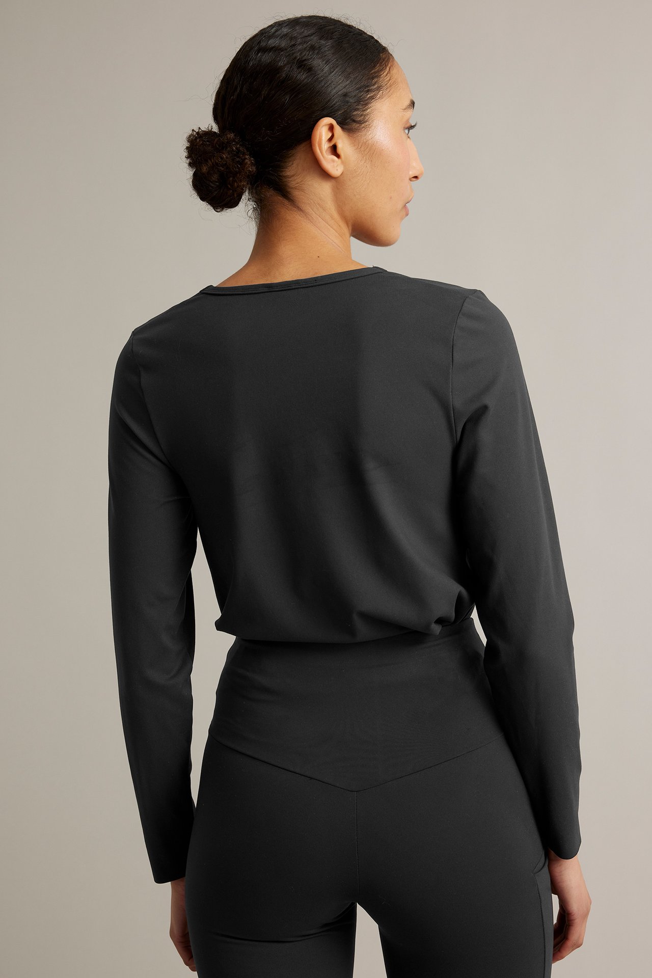 Ryggvy av en kvinna i svart långärmad träningströja och matchande svarta träningstights.