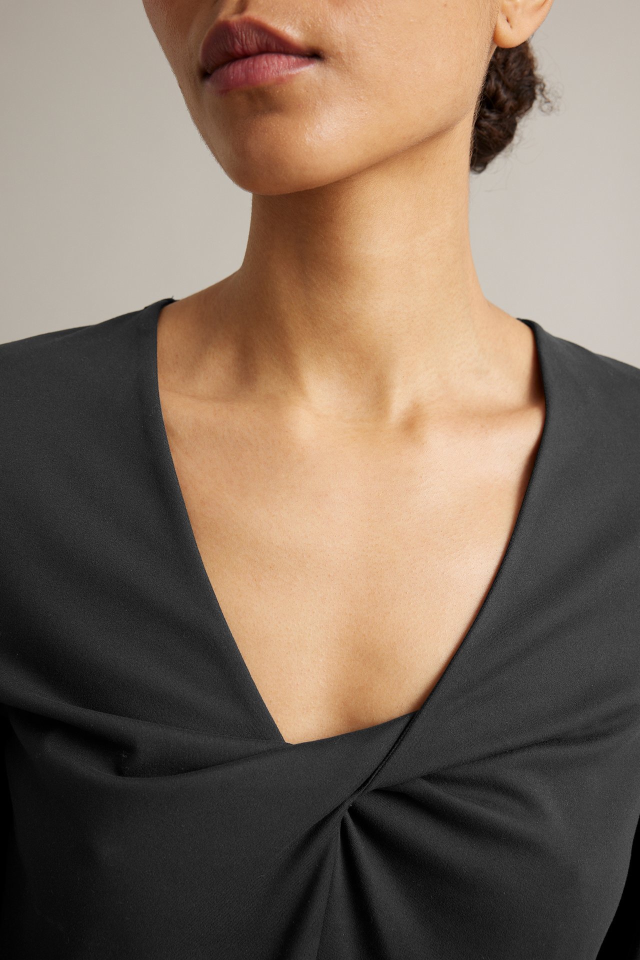 Närbild, framifrån, av en kvinna i en svart träningstopp i jersey med knuten v-ringning.