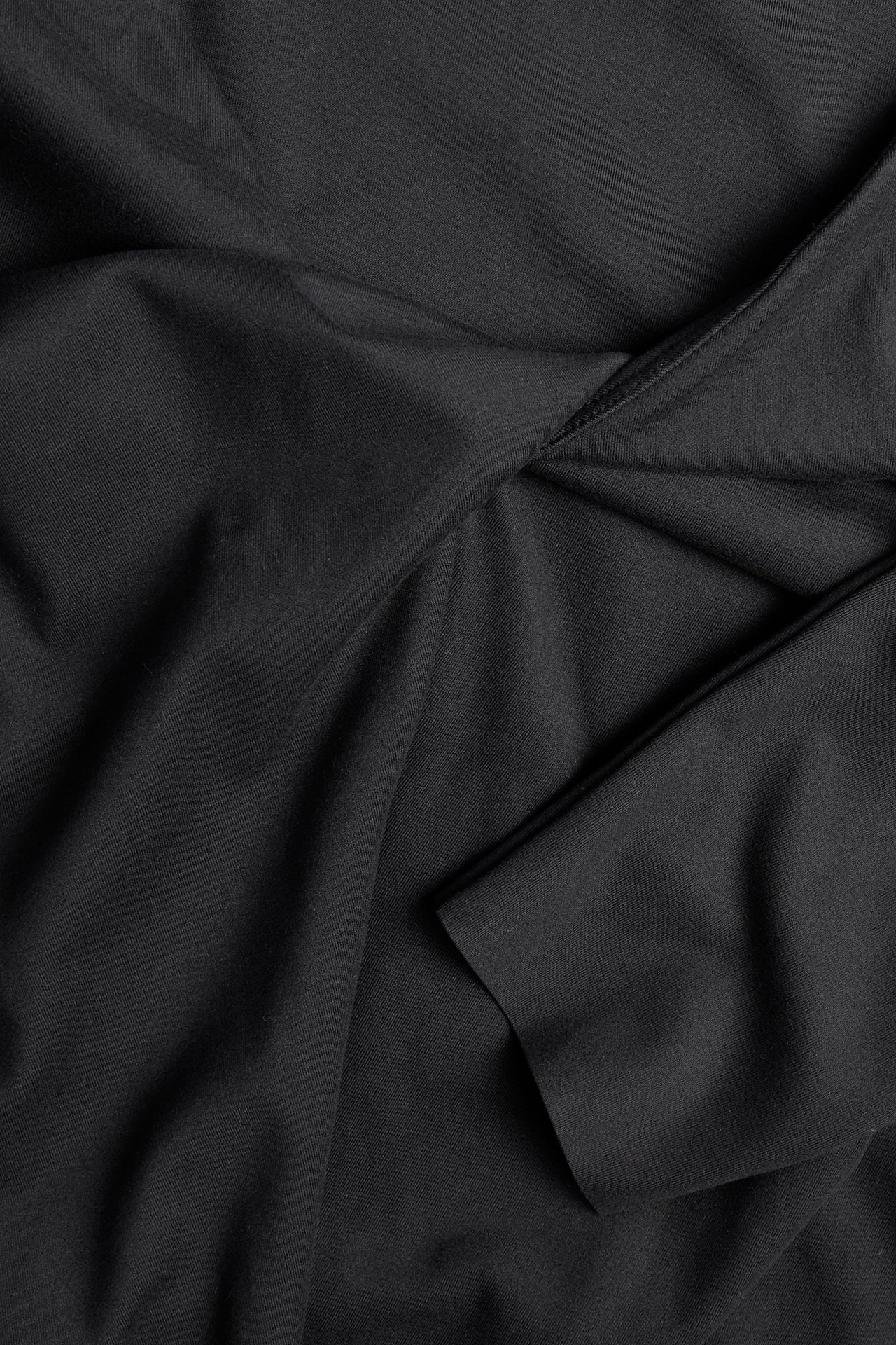 Nærbilde, flat lay av svart jerseytreningstopp med omslag og knute i v-halsen.