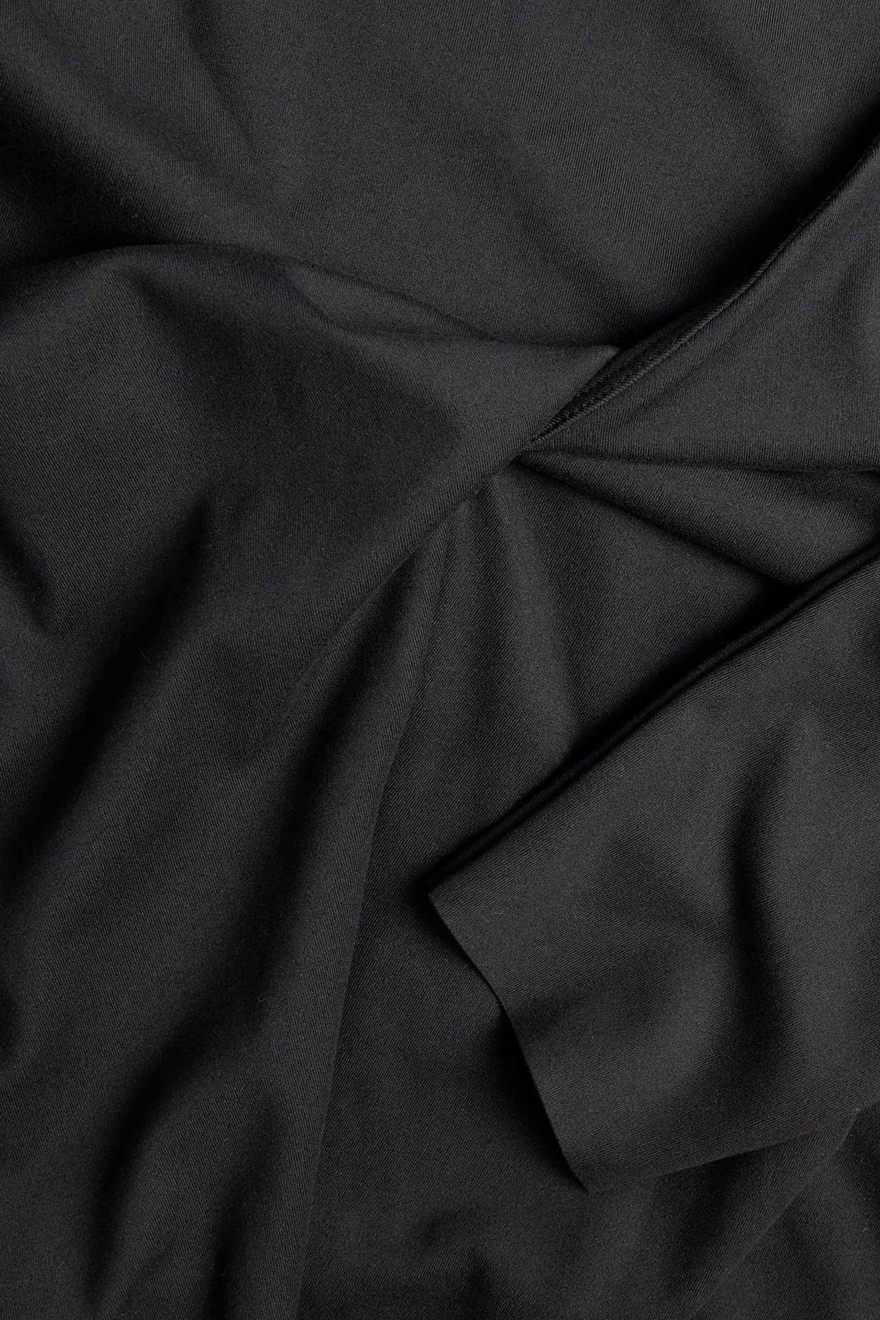 Nærbilde, flat lay av svart jerseytreningstopp med omslag og knute i v-halsen.