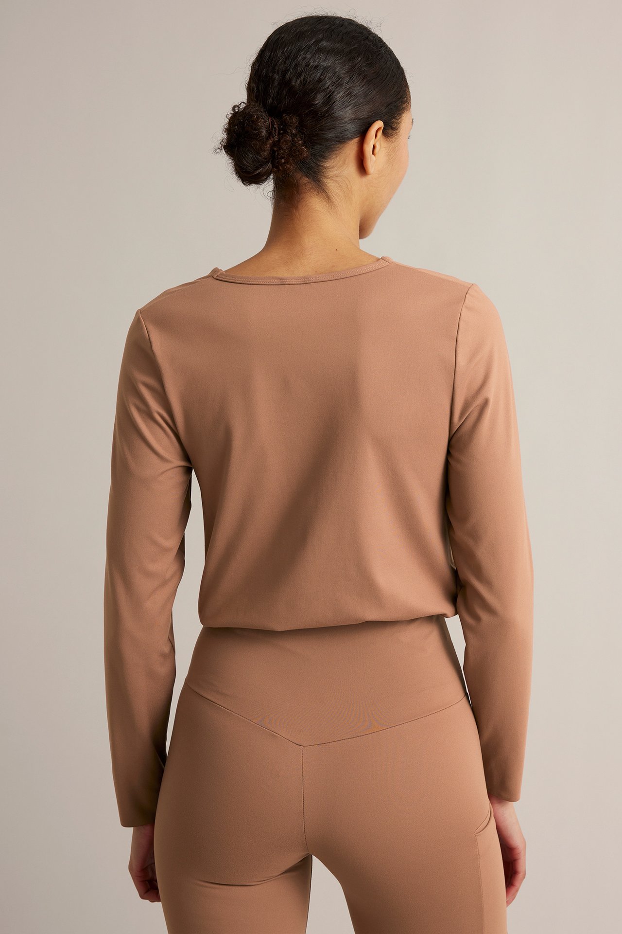 Ryggvy av en kvinna i en långärmad brun träningströja och matchande bruna träningstights.