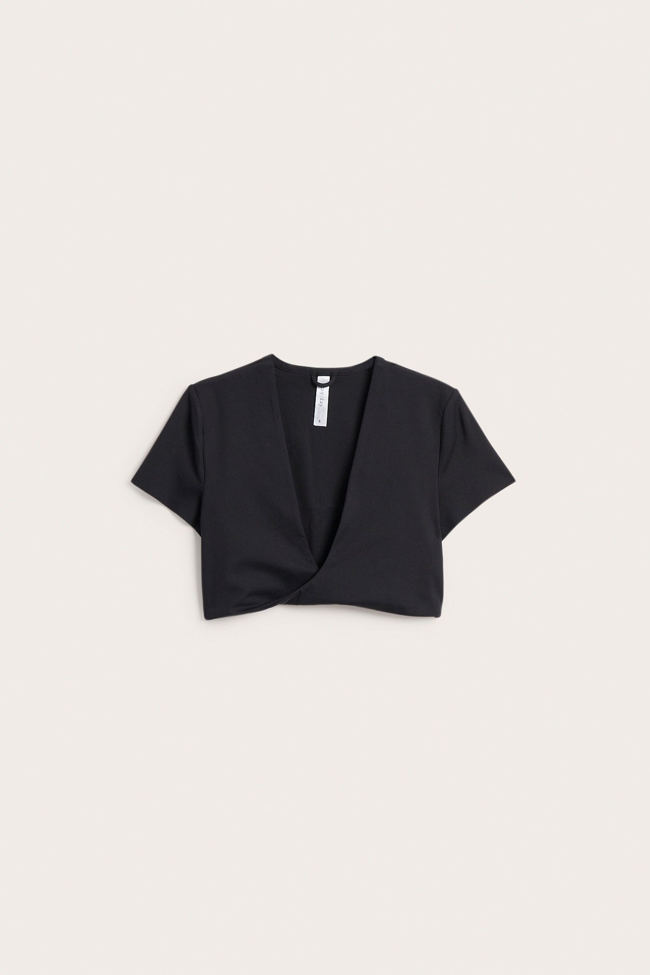 Framsida av en svart, enfärgad, kort topp i mjuk stretchjersey med vriden djup V-ringning.