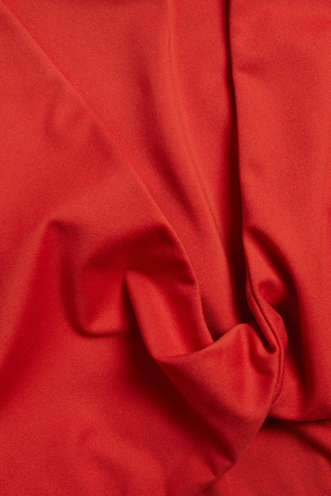 Närbild av ett mjukt, matt rött stretchjerseytyg från en topp, med veck.