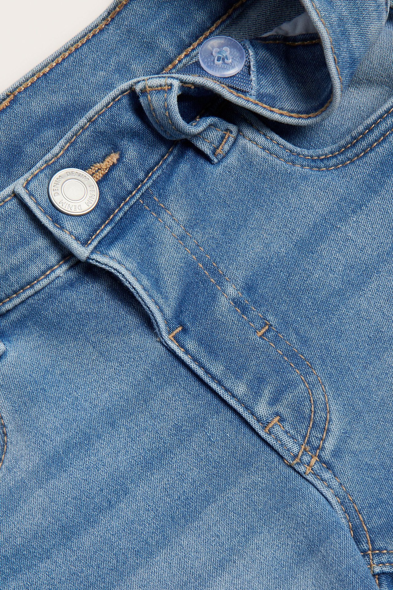 Zbliżenie na jasnoniebieskie dziecięce szorty dżinsowe, z srebrnym guzikiem i wewnętrzną regulacją talii.