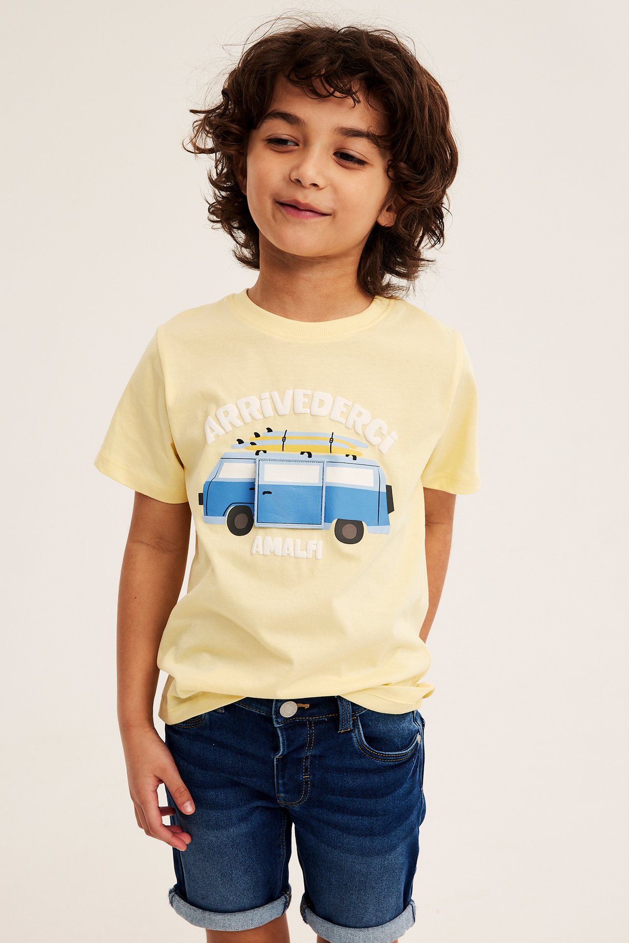 Frontvy av ett barn i mörka denimtrikåshorts med upprullade benslut och gul grafisk t-shirt.