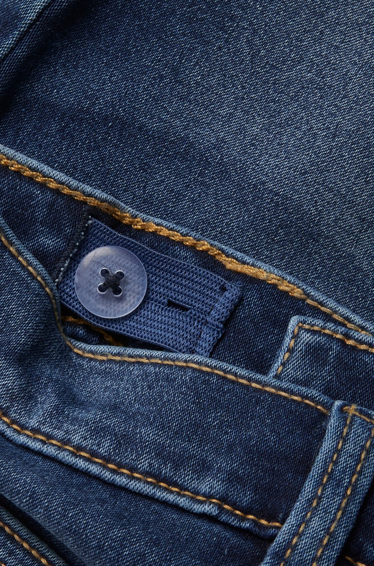 Närbild av mörkblå jeansshorts med justerbar innerlinning och en genomskinlig knapp.