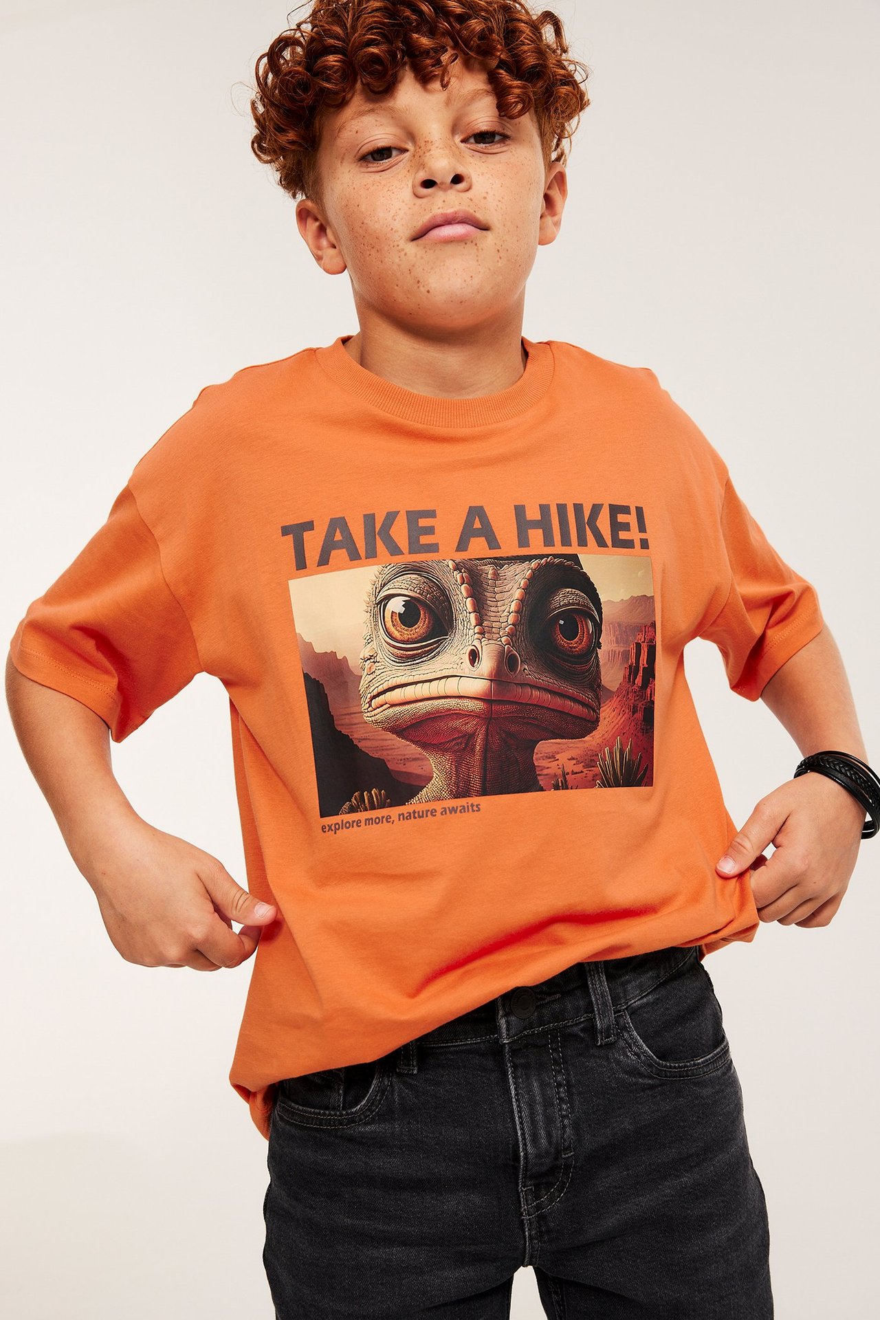 Chłopiec w pomarańczowej koszulce z nadrukiem, krótkie rękawy, przód.