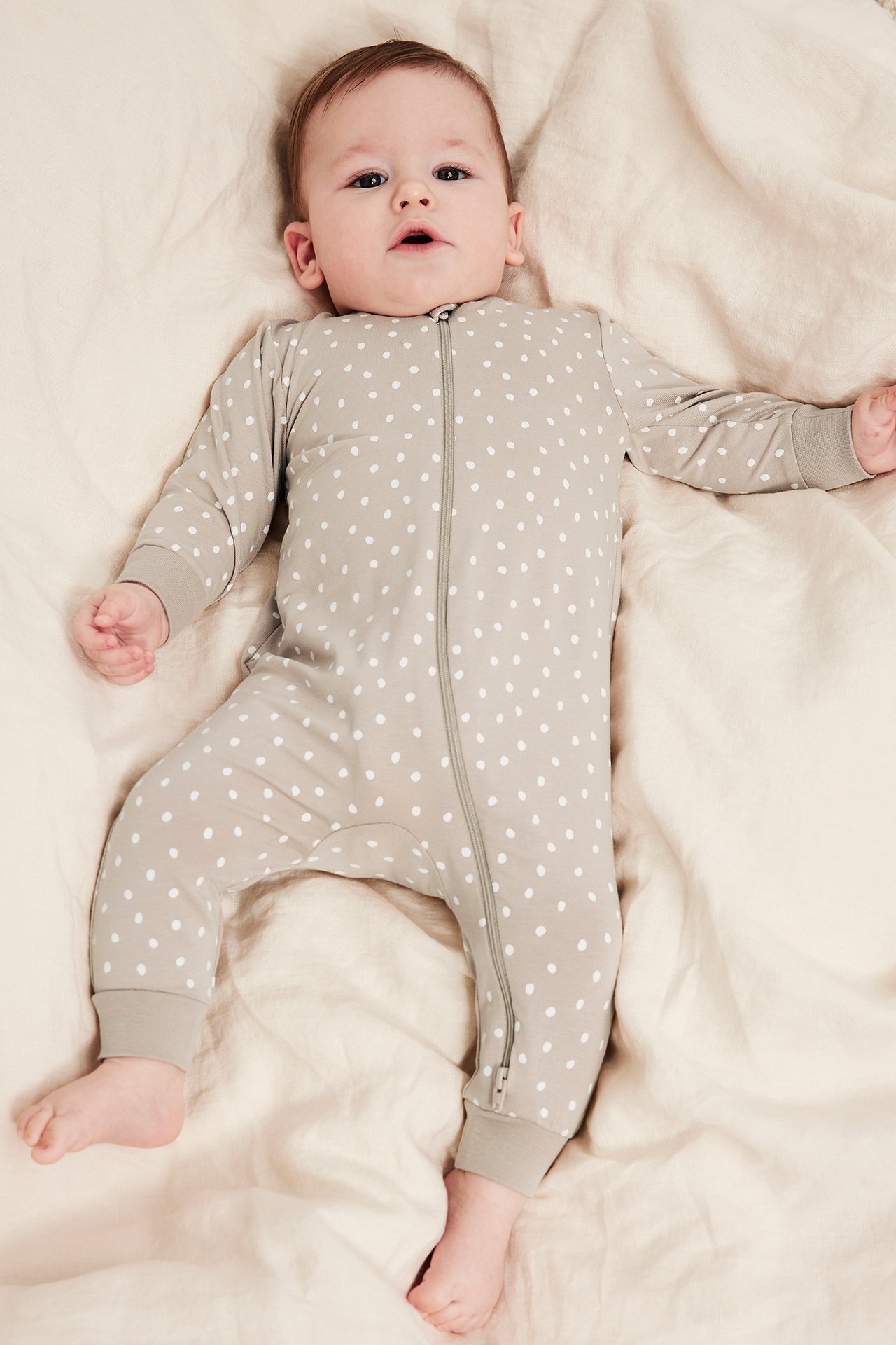 Widok z przodu: niemowlę w beżowym bawełnianym pajacyku w białe kropki, z dwukierunkowym zamkiem.