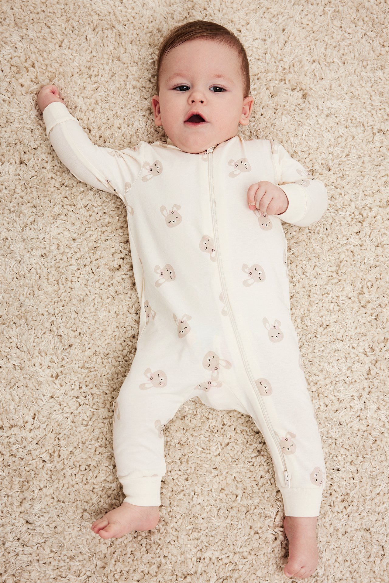 Widok z góry na niemowlę w kremowym pajacyku z nadrukiem królików i dwukierunkowym zamkiem.