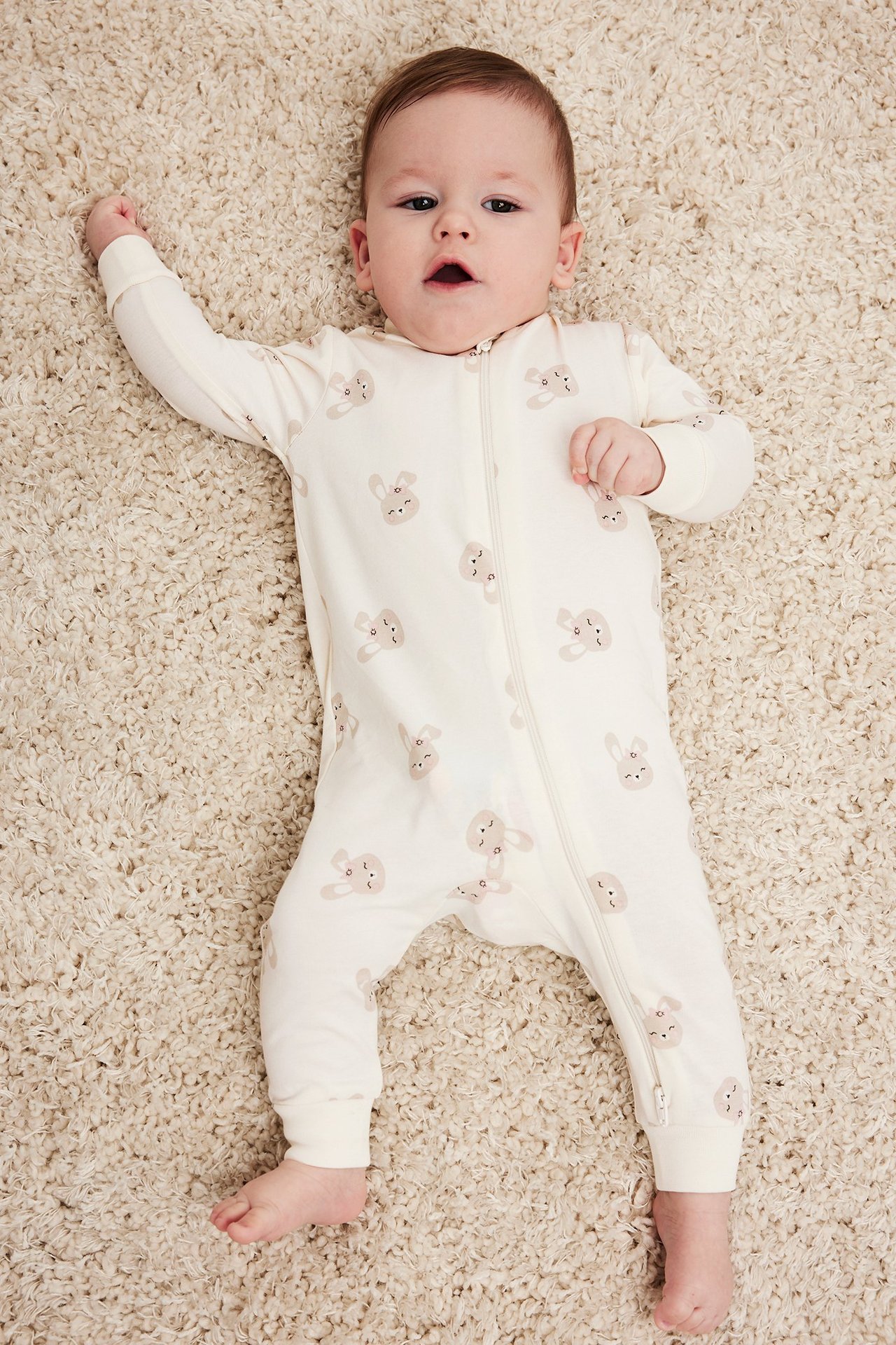 Widok z góry na niemowlę w kremowym pajacyku z nadrukiem królików i dwukierunkowym zamkiem.