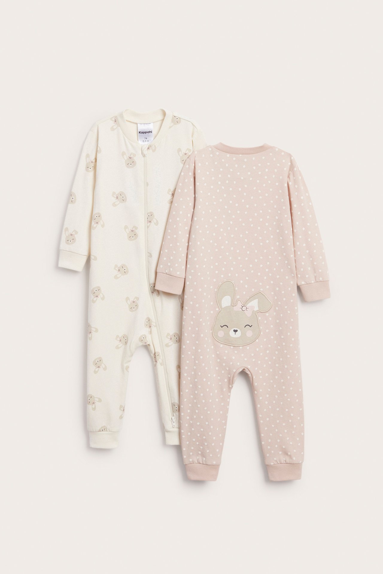 Widok z przodu dwóch śpioszków dla niemowląt: beżowy w króliczki i różowy w kropki z aplikacją królika.