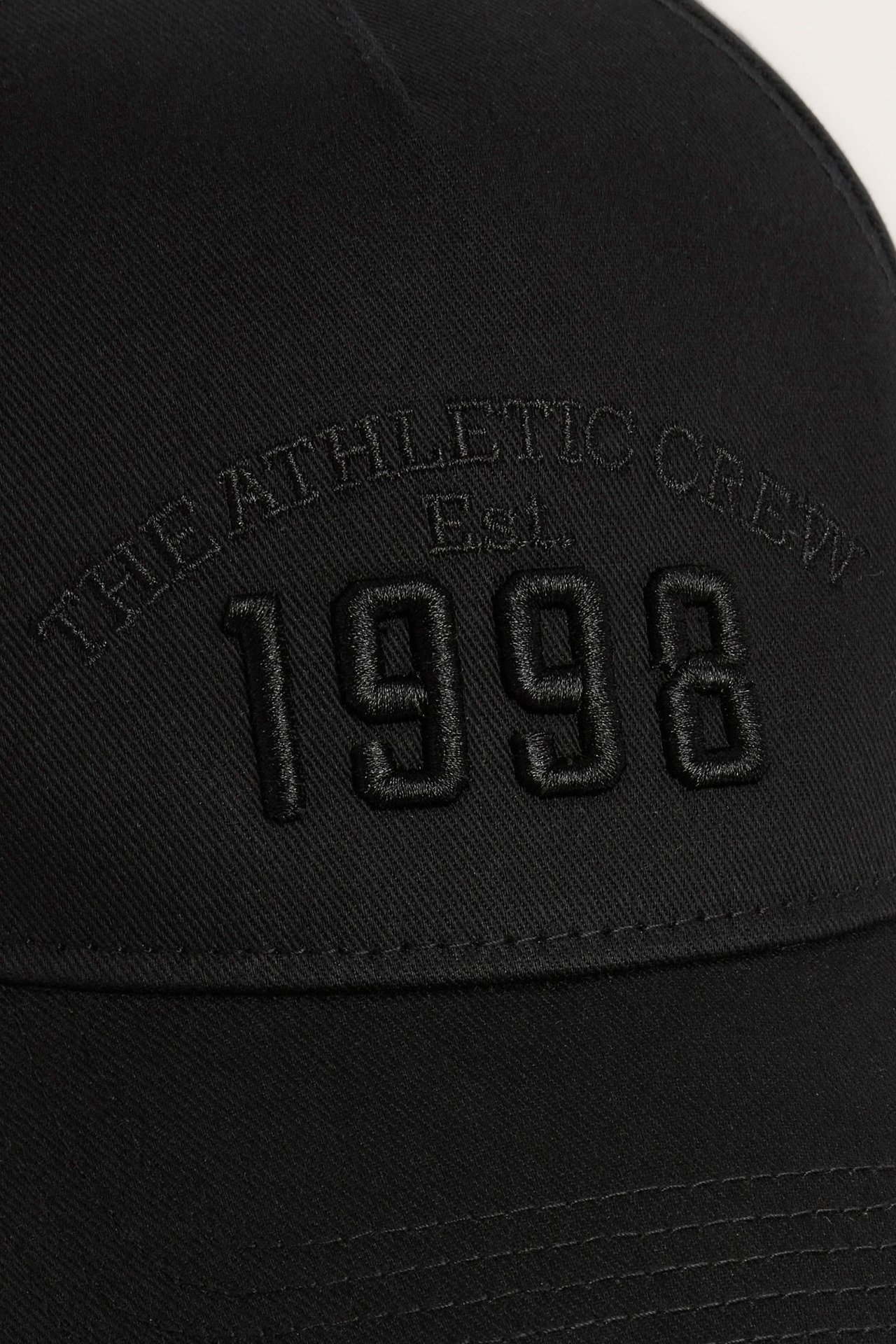 Zbliżenie przodu czarnej czapki z bawełnianego twillu z haftem "THE ATHLETIC CREW Est. 1998".