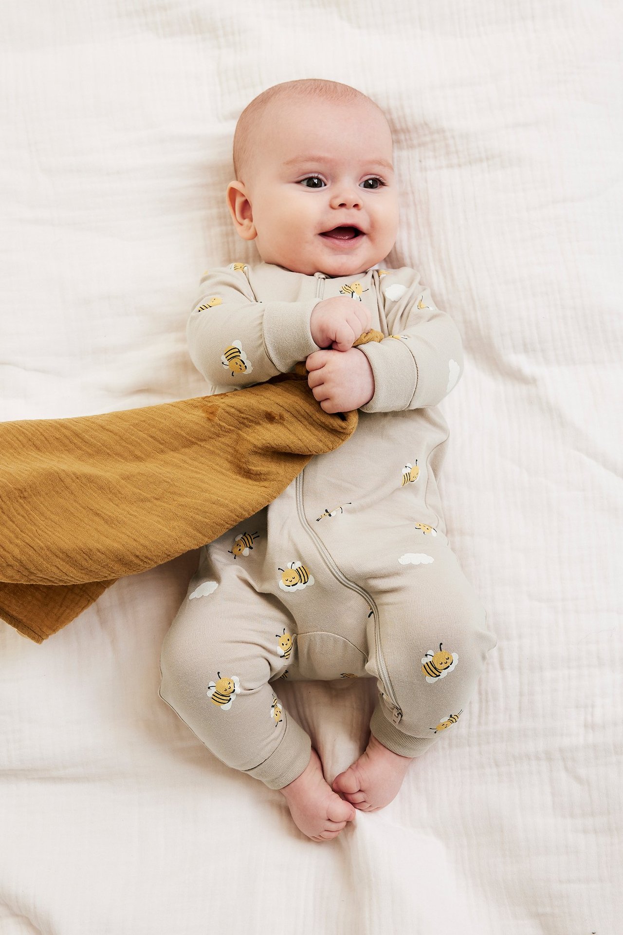 Widok z góry na niemowlę w beżowym pajacyku w pszczółki z dwukierunkowym zamkiem, trzymające brązowy materiał.