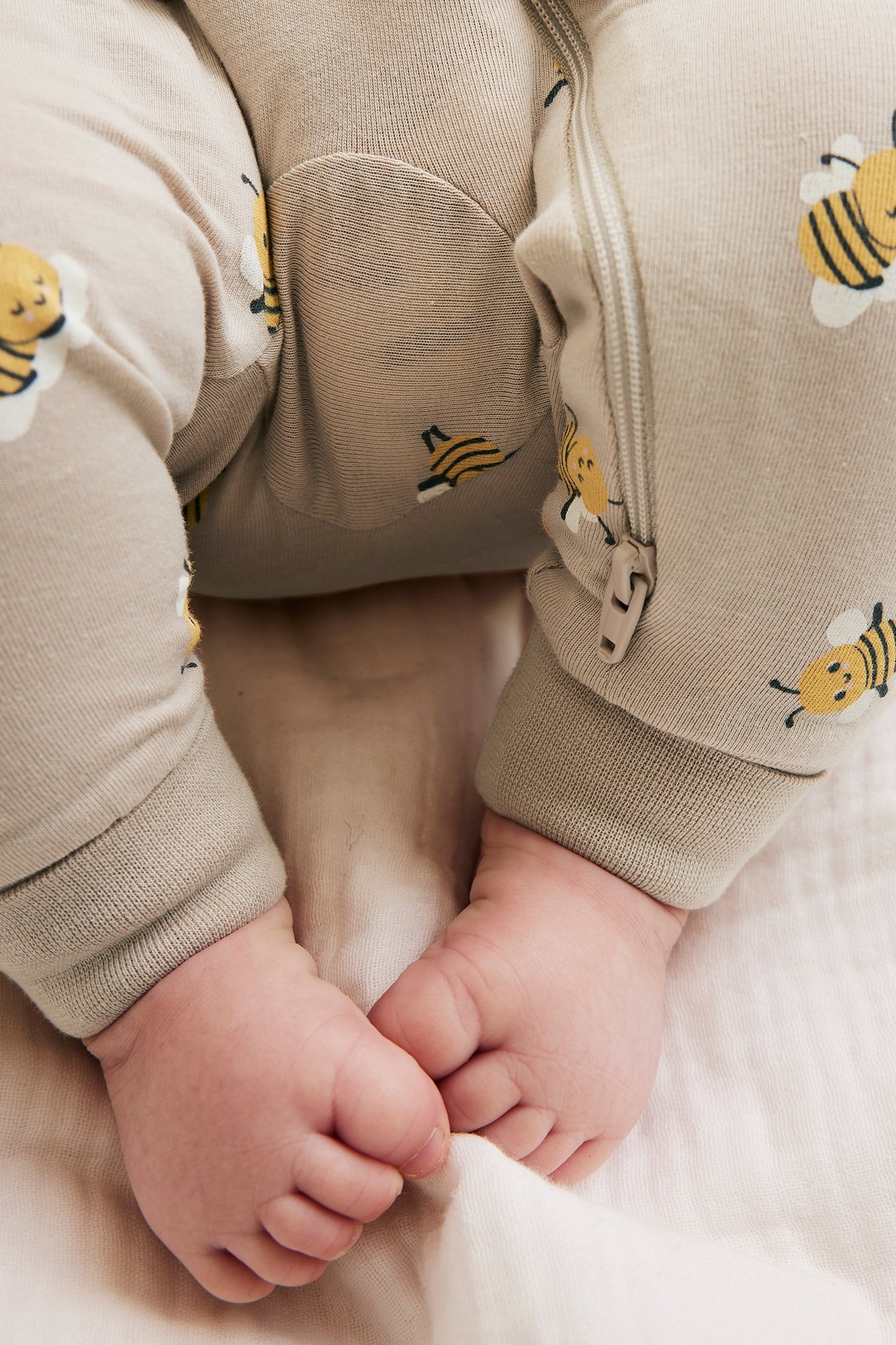 Zbliżenie niemowlaka w beżowym wzorzystym pajacyku z żółtymi pszczołami i dwukierunkowym zamkiem.