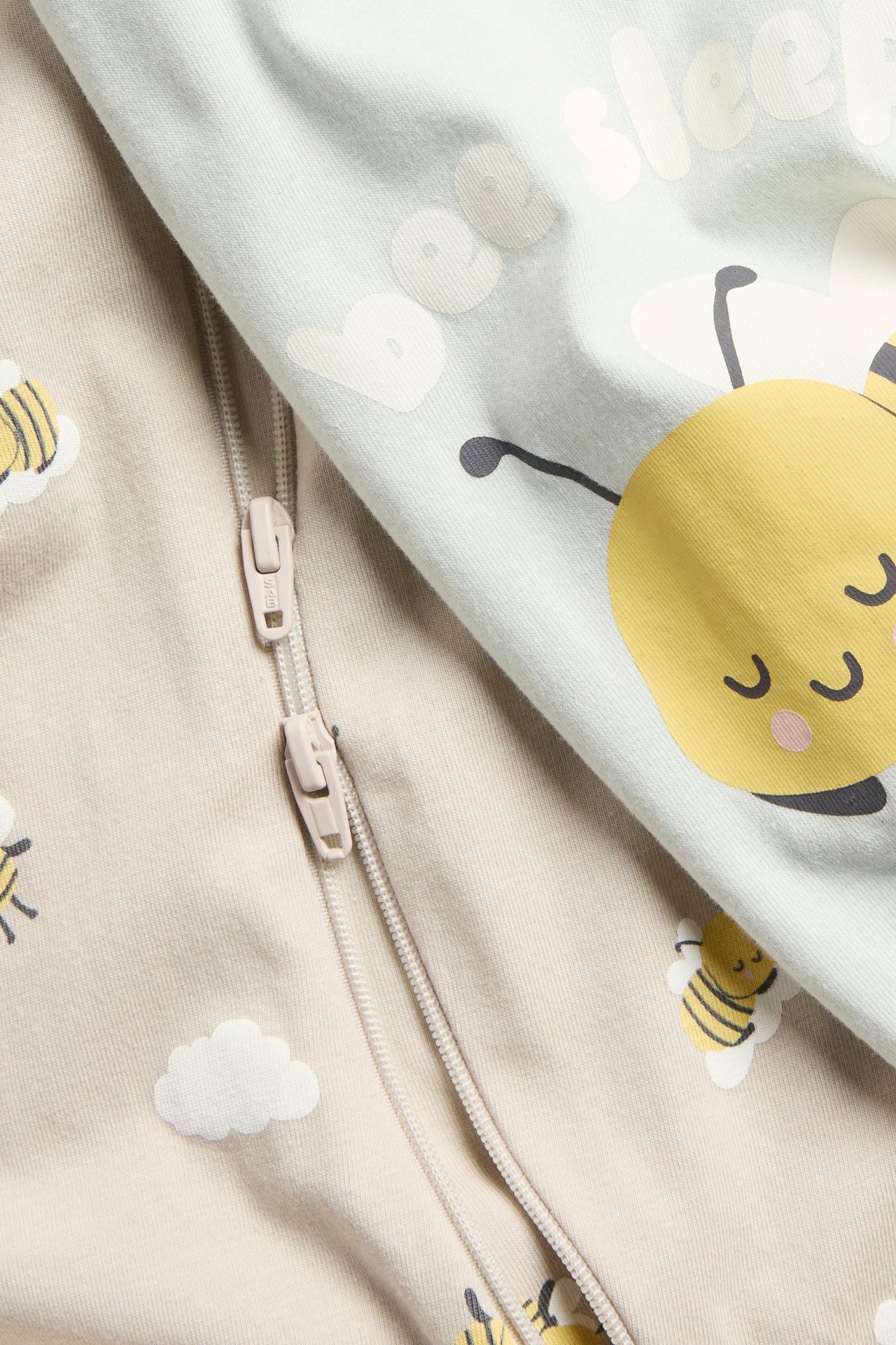 Zbliżenie na dwa pajace niemowlęce: beżowy w pszczoły z zamkiem dwukierunkowym, jasnozielony z pszczołą.