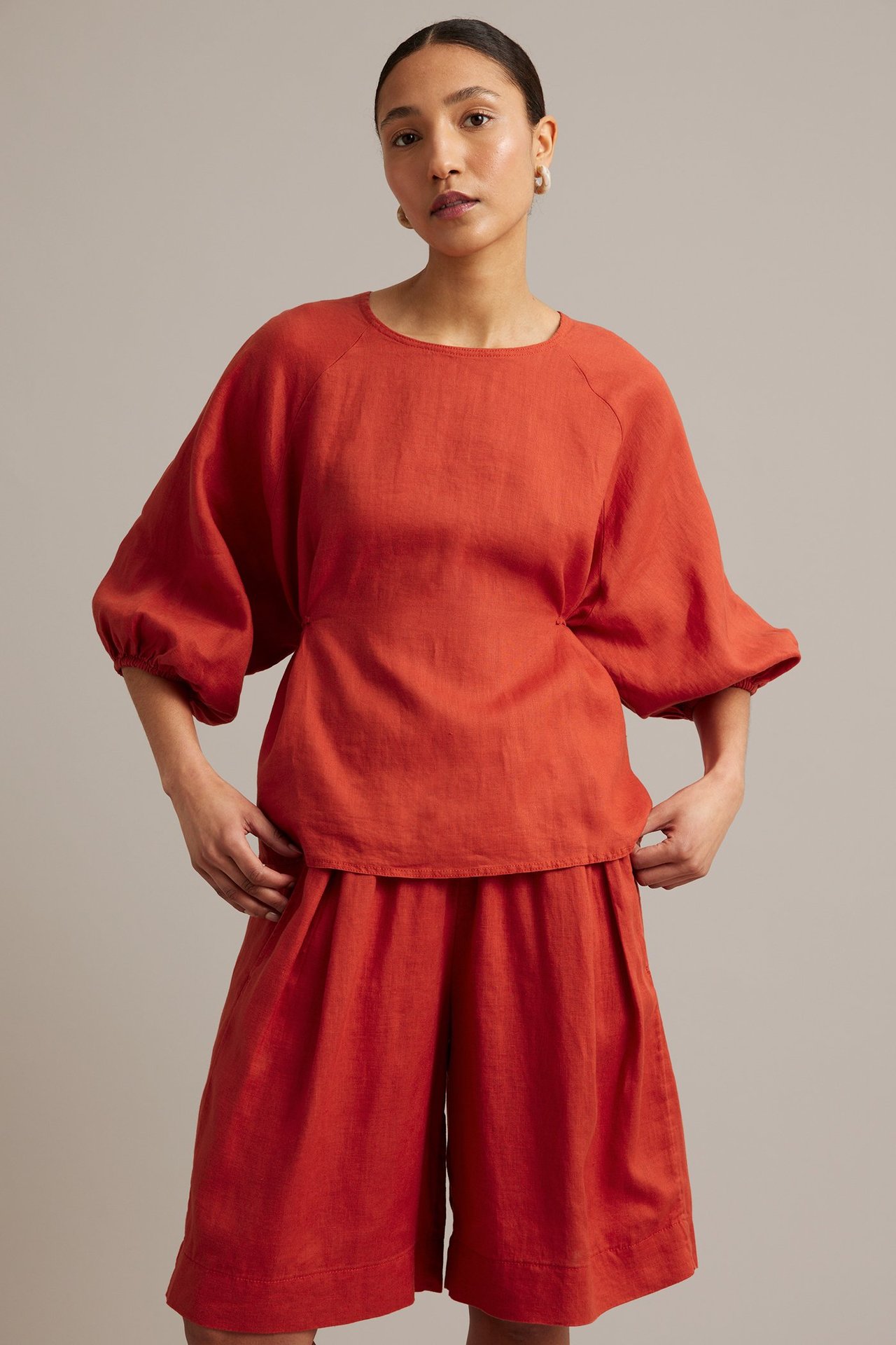 Framifrån: kvinna i röd linneblus med vida raglanärmar och matchande röda linneshorts med vida ben.