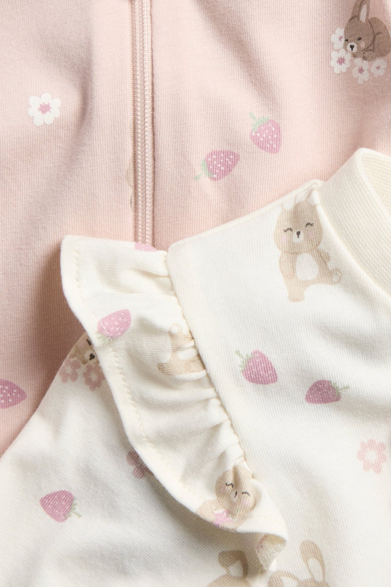 Zbliżenie na ecru rampers niemowlęcy z falbanami na ramionach i wzorem w króliki, obok różowy rampers na zamek.