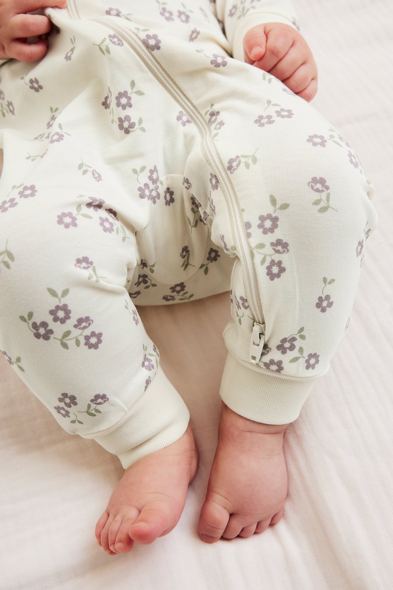 Zbliżenie na dziecko w kremowym pajacyku z liliowym kwiatowym wzorem i dwukierunkowym zamkiem.