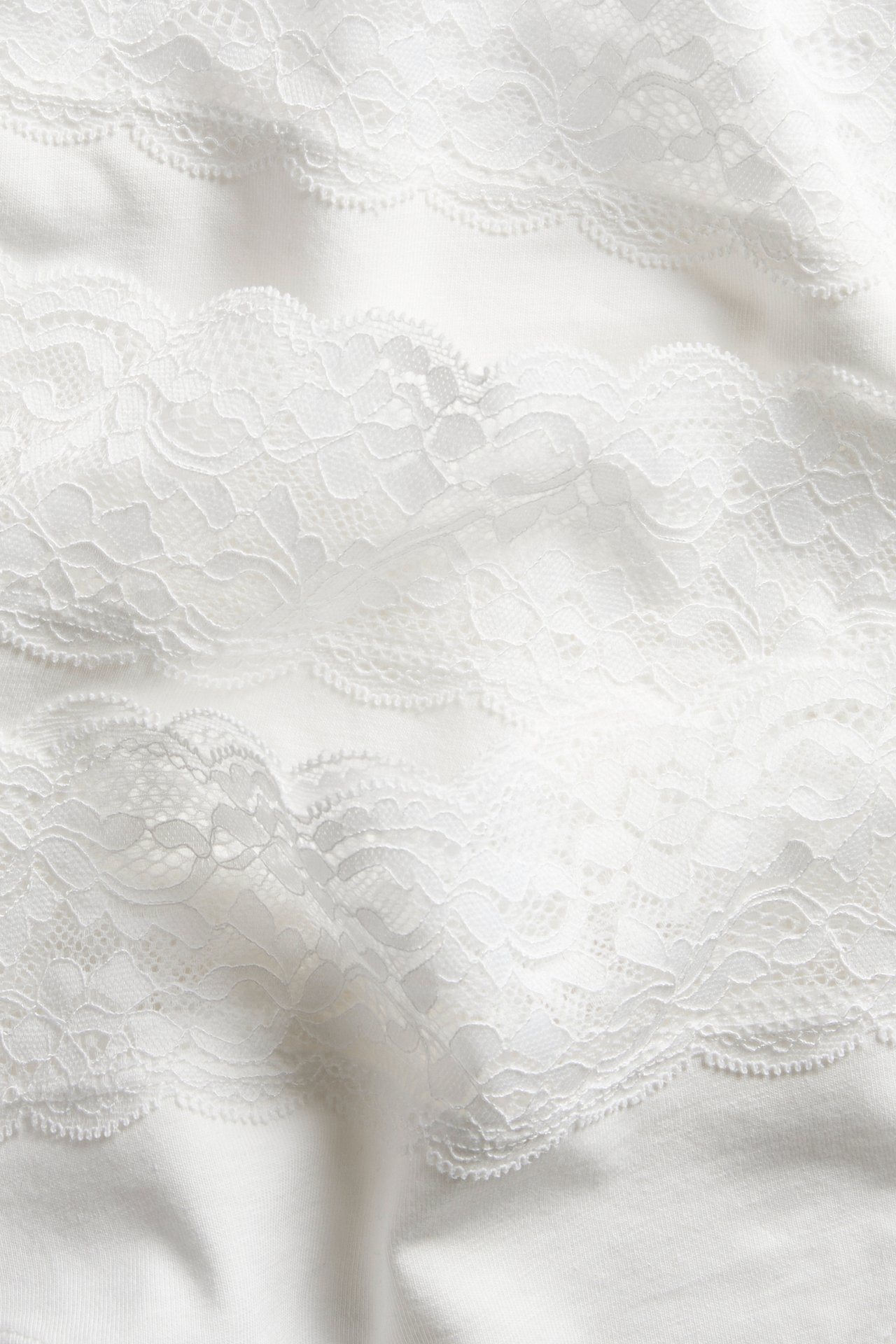 Nærbilde av hvit bomullsstringtruse med intrikate hvite blondedetaljer.